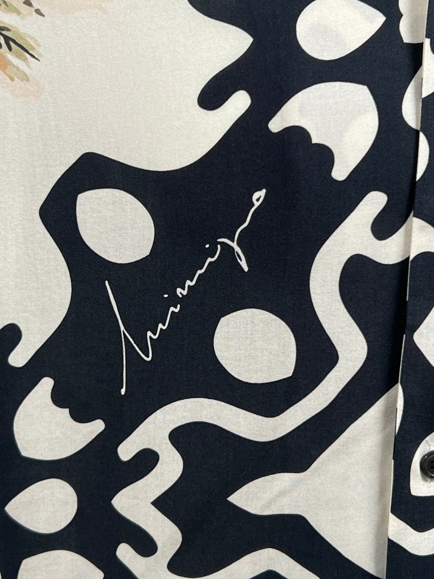 Close-up of a fabric with an abstract navy and white pattern, reminiscent of a tropical print shirt. Part of the INIMIGO collection, this design features an intricate signature that adds a unique touch to the INIMIGO ISH3525 PALM SHIRT BLACK.
