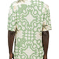 A person wears the Inimigo ISH3525 Palm Shirt Green by INIMIGO, a short-sleeve tropical shirt showcasing a green and white abstract pattern with a palm tree design on the back, perfectly matched with light-colored pants.