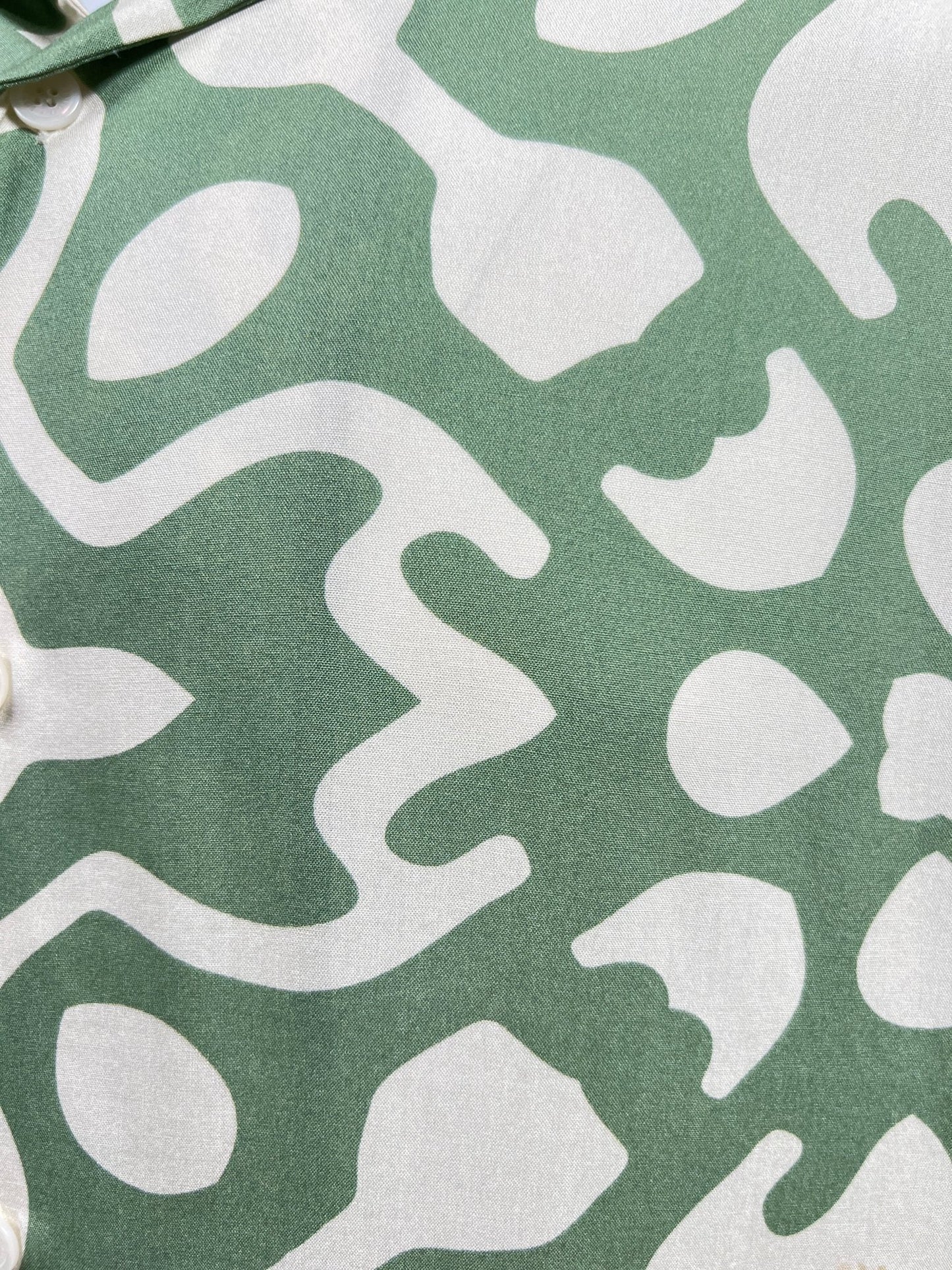 Close-up of a green fabric with a white abstract pattern and buttons along the edge, reminiscent of an INIMIGO ISH3525 PALM SHIRT GREEN by INIMIGO, perfect for any occasion.