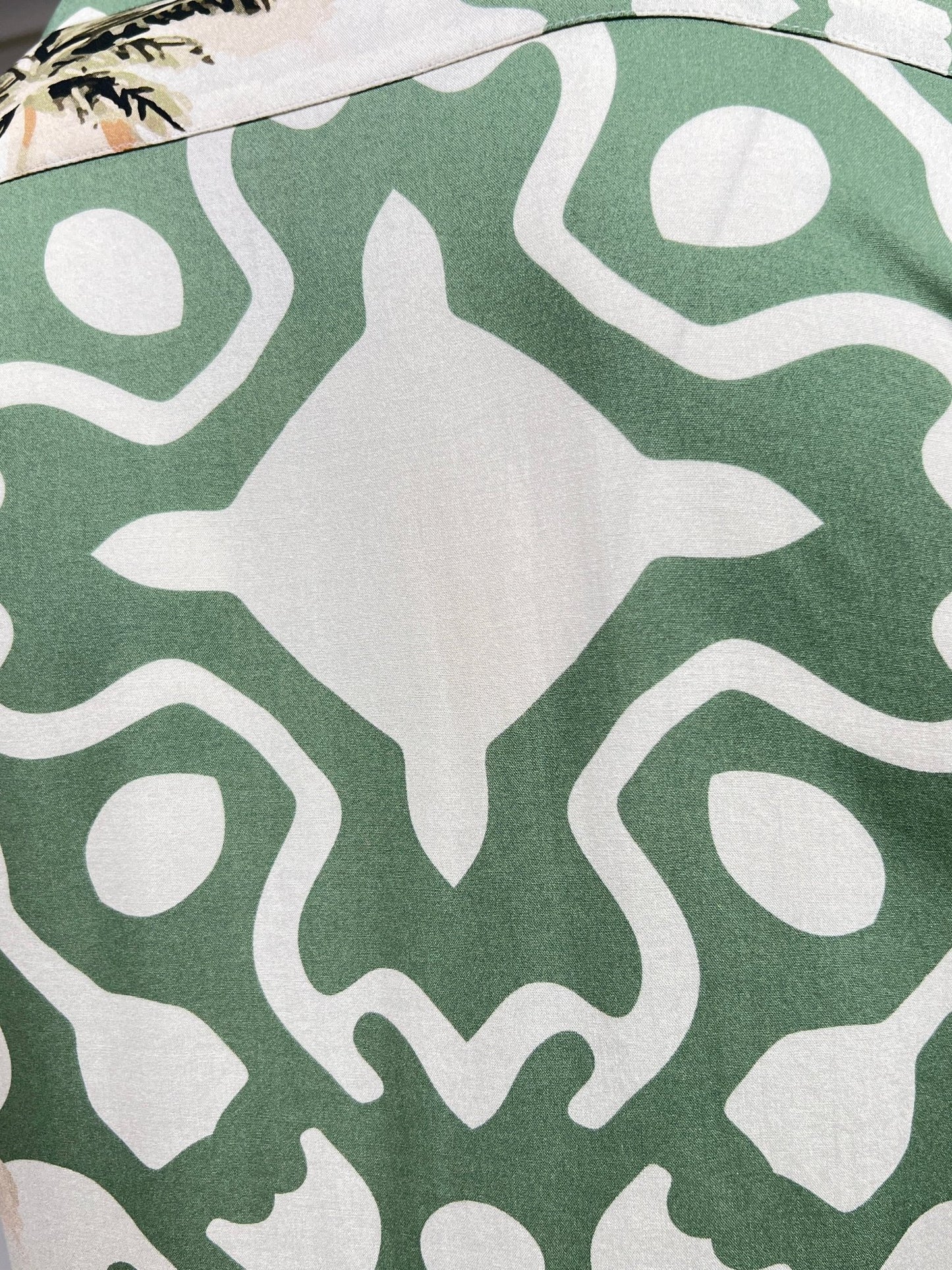 A close-up of the INIMIGO ISH3525 PALM SHIRT GREEN, featuring a green fabric with a symmetrical white pattern, reminiscent of a tropical print shirt.