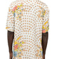 A person is wearing the INIMIGO ISH3528 Heart Birds Shirt Raw, a white short-sleeved button-up adorned with polka dots and vibrant abstract patterns. This stylish shirt is paired with tan pants and viewed from the back.