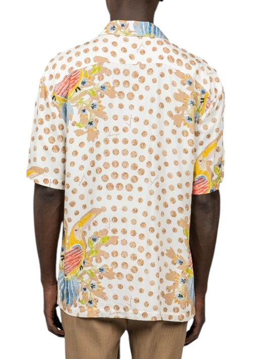 A person is wearing the INIMIGO ISH3528 Heart Birds Shirt Raw, a white short-sleeved button-up adorned with polka dots and vibrant abstract patterns. This stylish shirt is paired with tan pants and viewed from the back.