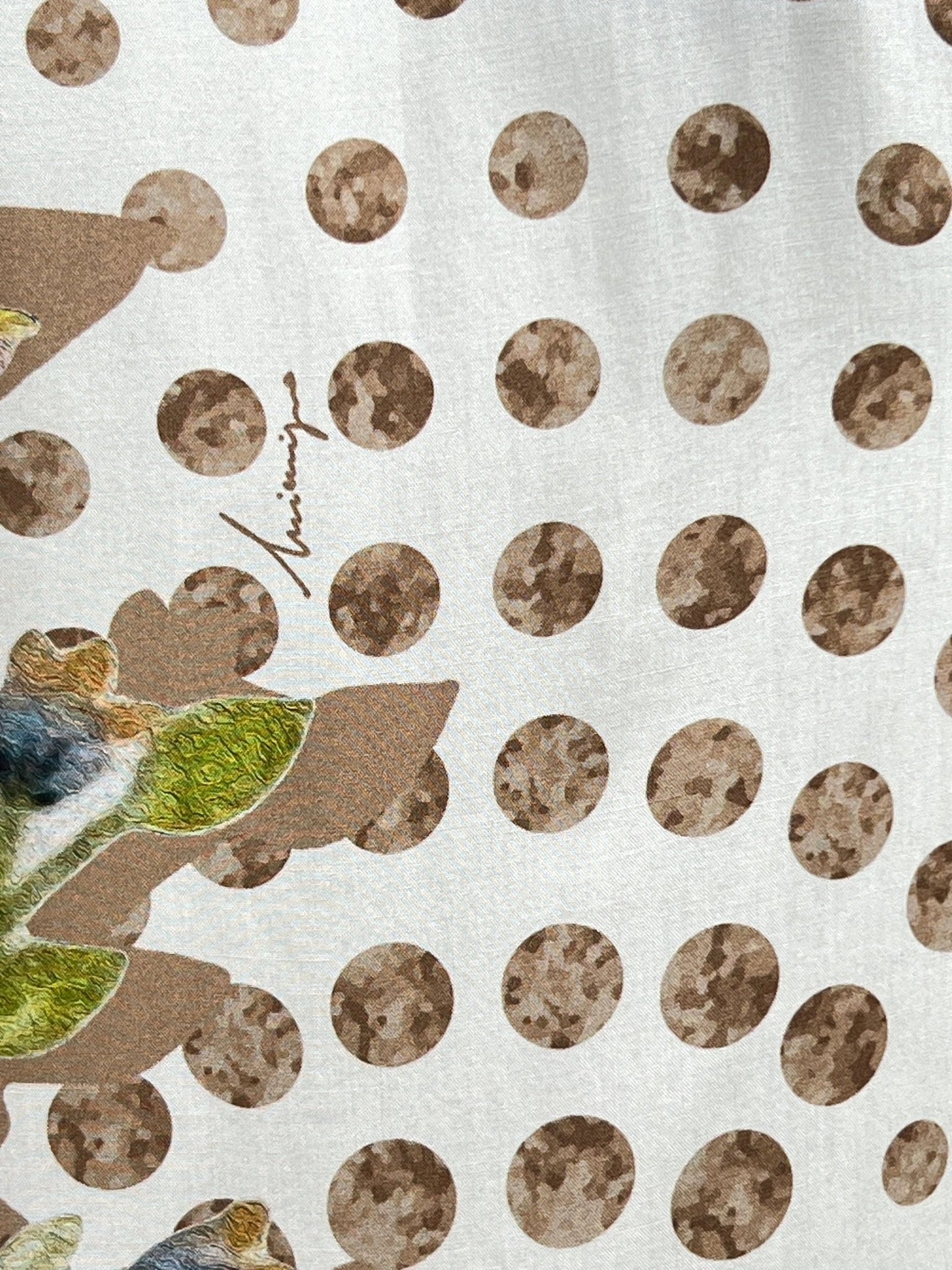 Close-up of fabric with a pattern of brown polka dots and green leaves, showcasing a unique all-over print. A signature is visible among the dots, hinting at the exclusivity of the INIMIGO ISH3528 HEART BIRDS SHIRT RAW by INIMIGO.