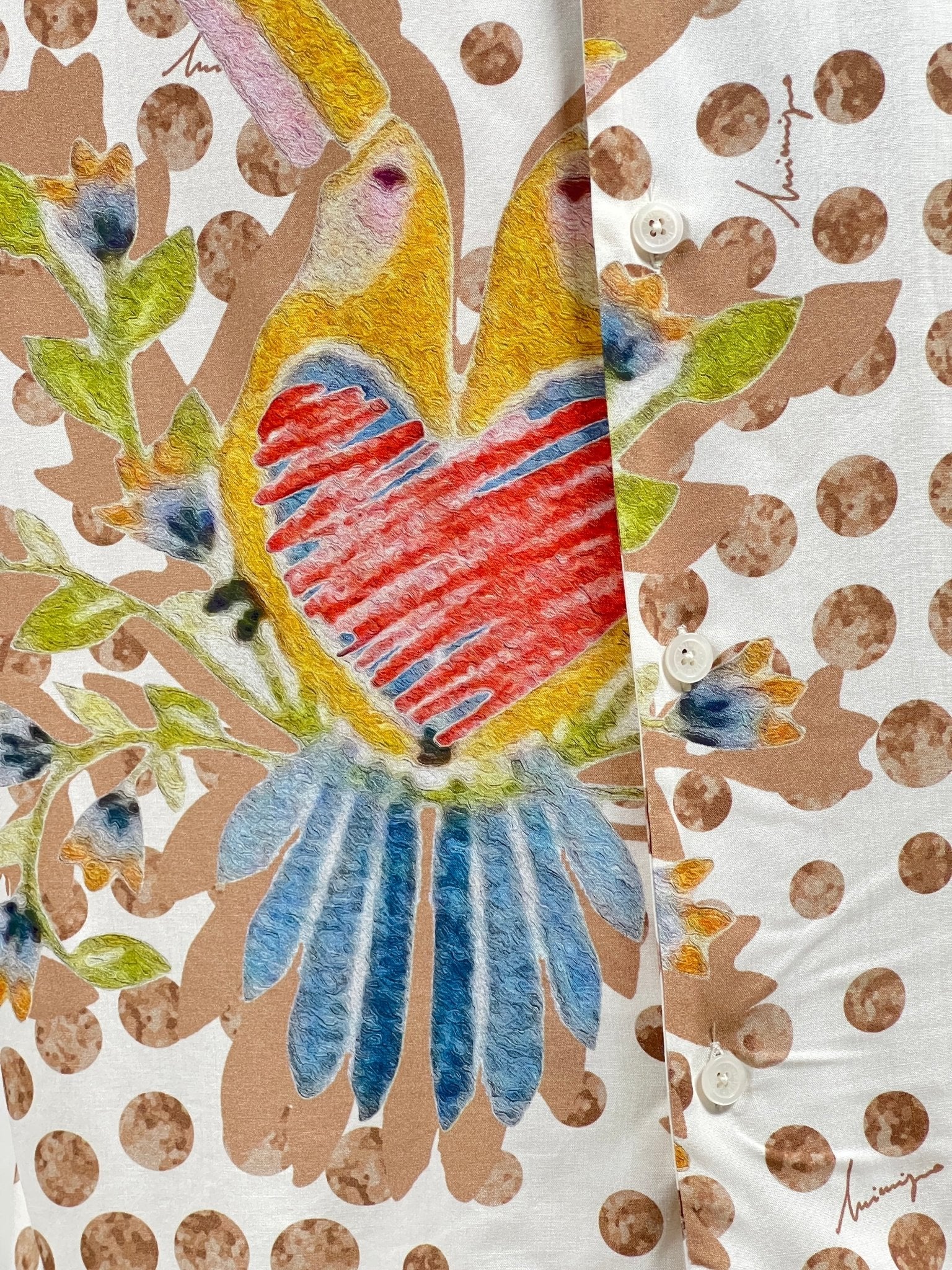 Close-up image of a fabric with a colorful bird design, featuring a red heart-shaped chest and blue tail feathers, set against a polka dot background with visible buttons—perfectly capturing the essence of our INIMIGO ISH3528 HEART BIRDS SHIRT RAW made from high-quality materials.