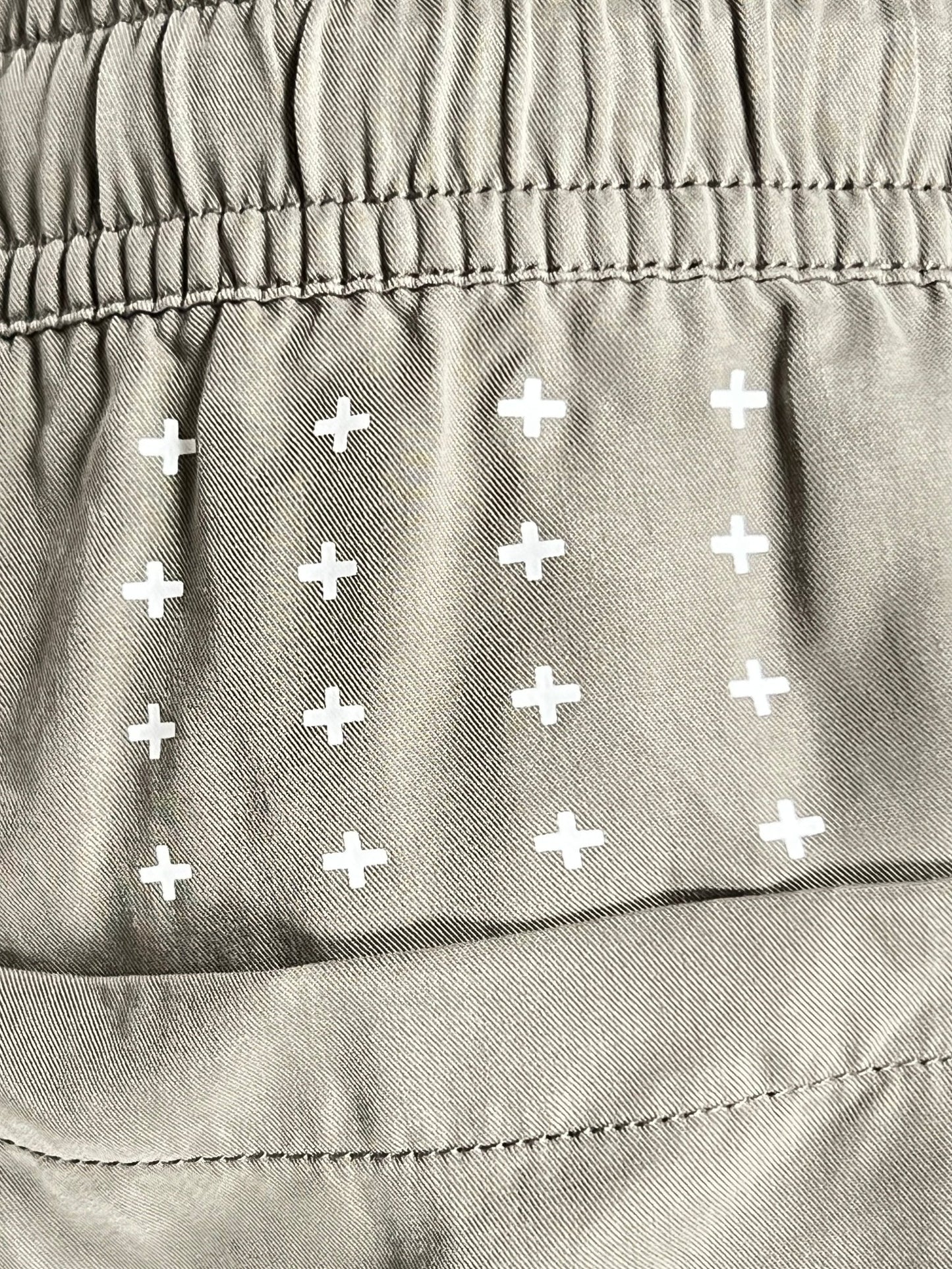 Close-up of khaki tencel fabric featuring an elasticated seam and white cross patterns, characteristic of the Ksubi logo on the KSUBI 1999 LIFE SHORT OUTBACK GREEN.