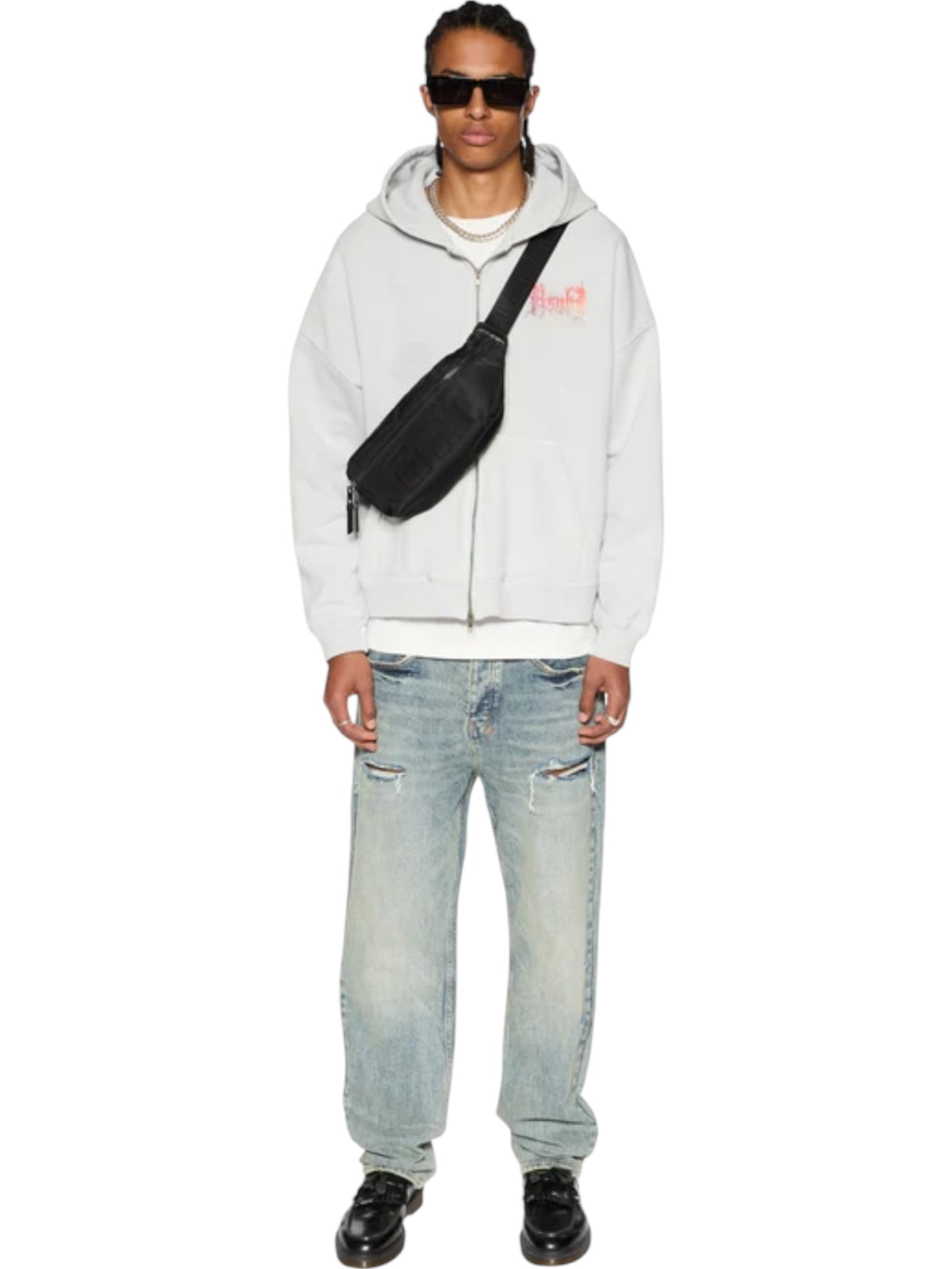 A person in sunglasses, a white hoodie, black shoes, and a crossbody bag stands against a white background wearing Ksubi Anti K Rogue Blue Trashed Denim. The KSUBI branded hardware distinguishes the look.