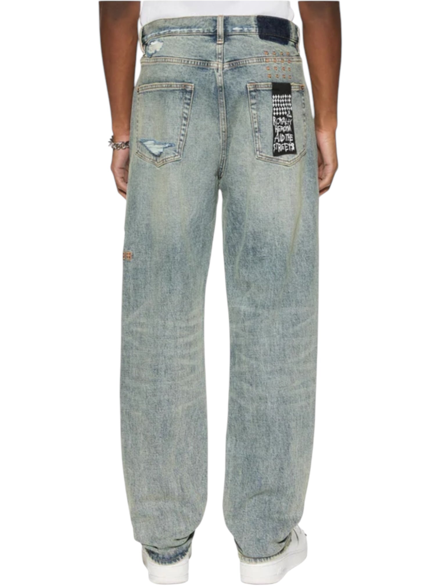 Seen from behind, someone wears Ksubi Anti K Rogue Blue Trashed Denim with distinct distressing and patches. The look is finished with white sneakers and subtle Ksubi-branded hardware for added flair.