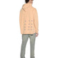 A person wearing a sun-faded KSUBI APEX BIGGIE HOODIE FLARE ORANGE with a pattern of plus signs on the back, grey pants, and white shoes, standing and facing away. This streetwear look is both casual and effortlessly stylish.