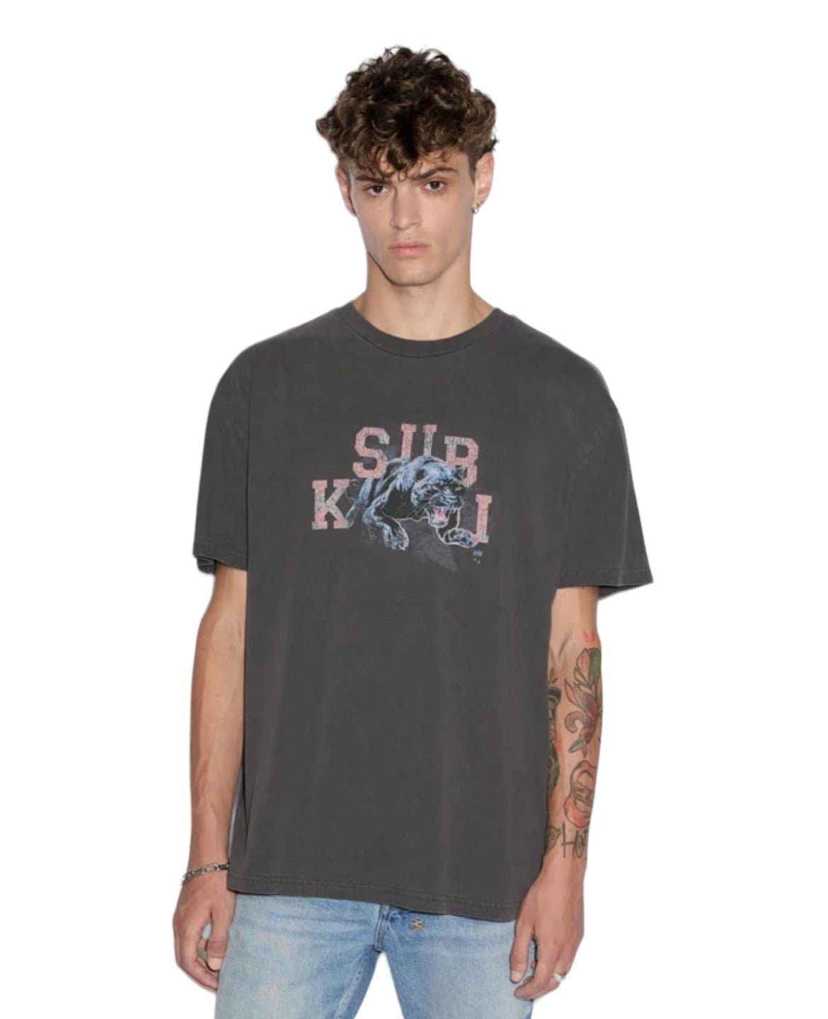 Dressed in a Ksubi Apex Biggie Ss Tee in faded black from the KSUBI brand, featuring an oversized fit with "SUB KULT" and a panther design, and paired with light blue jeans, this person stands against a plain white background, exuding effortless street style.