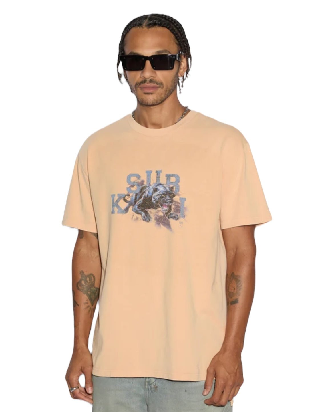 A person in sunglasses and light blue jeans wears a sun-faded KSUBI Apex Biggie SS Tee Flare Orange, featuring a graphic design, against a white background.