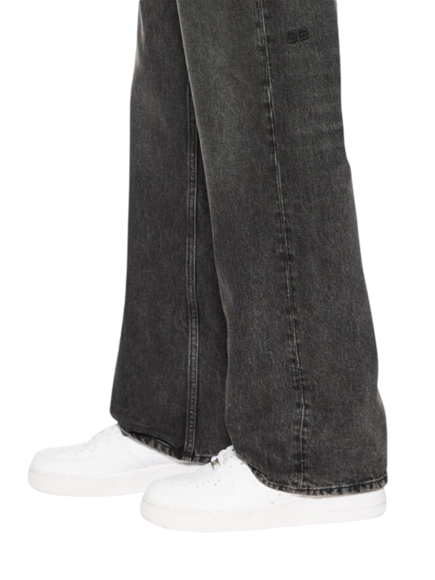 A person in Ksubi Bronko Blakk Rokk Black boot-cut jeans, made from premium rigid black denim and cropped at the knees, paired with white sneakers. Subtle Ksubi branded hardware adds a touch of style.