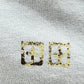 Close-up of a gray fabric from the KSUBI CLUBHOUSE BIGGIE TEE SHALLOWS BLU by KSUBI, showcasing premium cotton jersey with two square symbols featuring internal cross-like designs in yellow and black.