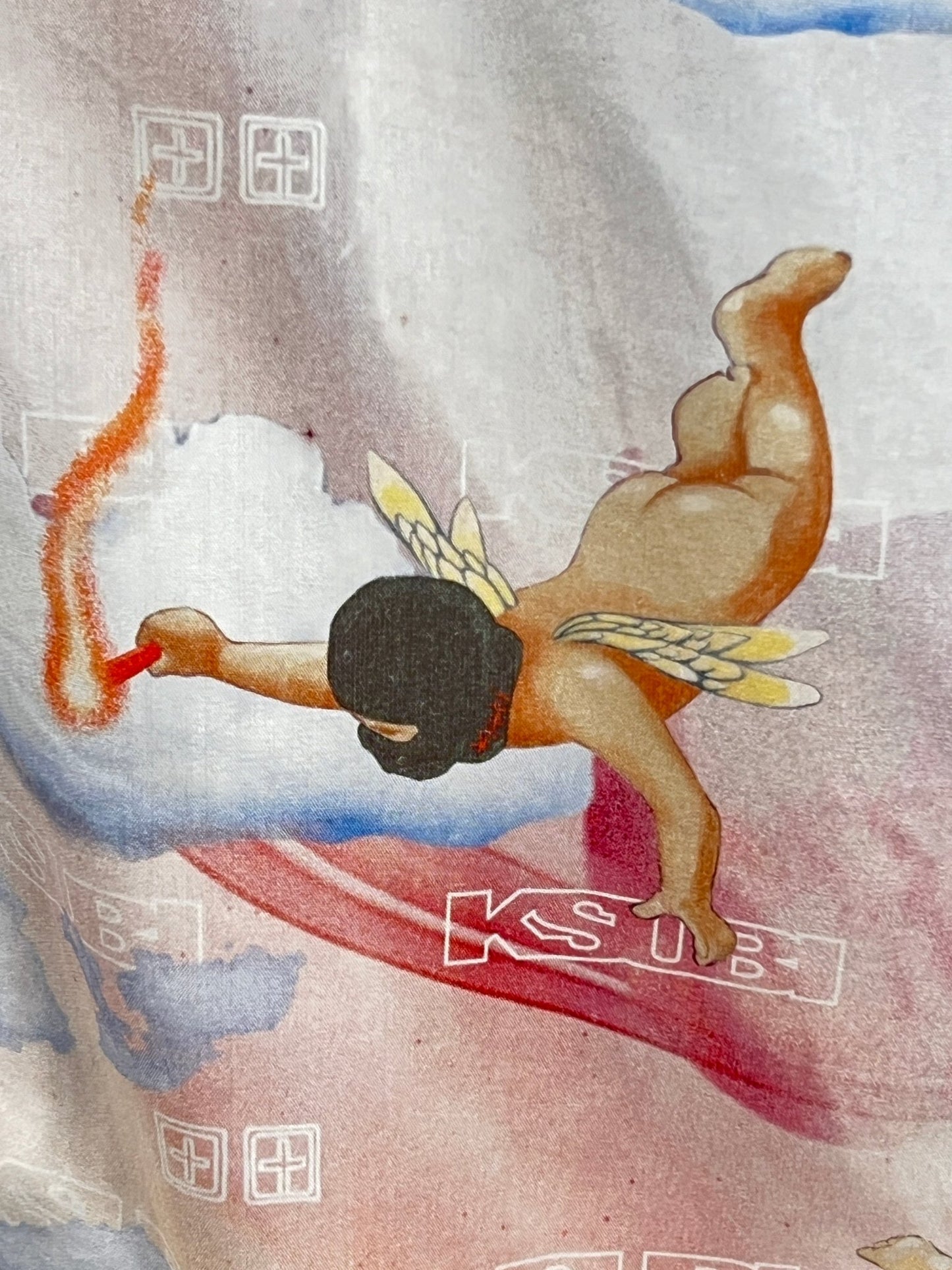 An ethereal winged figure spray paints a red line on a cloud, surrounded by abstract designs and "Ksubi" text, reminiscent of the Ksubi Dreamers Resort Shirt Multi. This whimsical scene captures the essence of a shirt crafted from soft Tencel fabric by KSUBI.