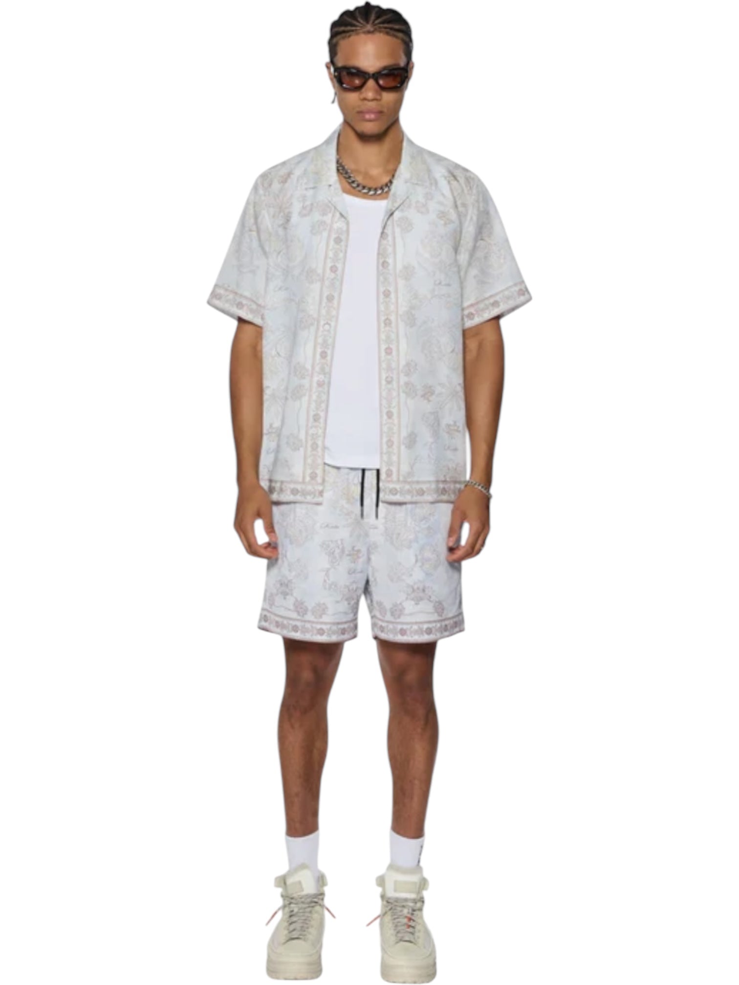 Man in KSUBI Eternity Boardshort Multi and matching short-sleeve shirt with subtle pattern, white undershirt, light sneakers, sunglasses, and jewelry, standing against a white background.