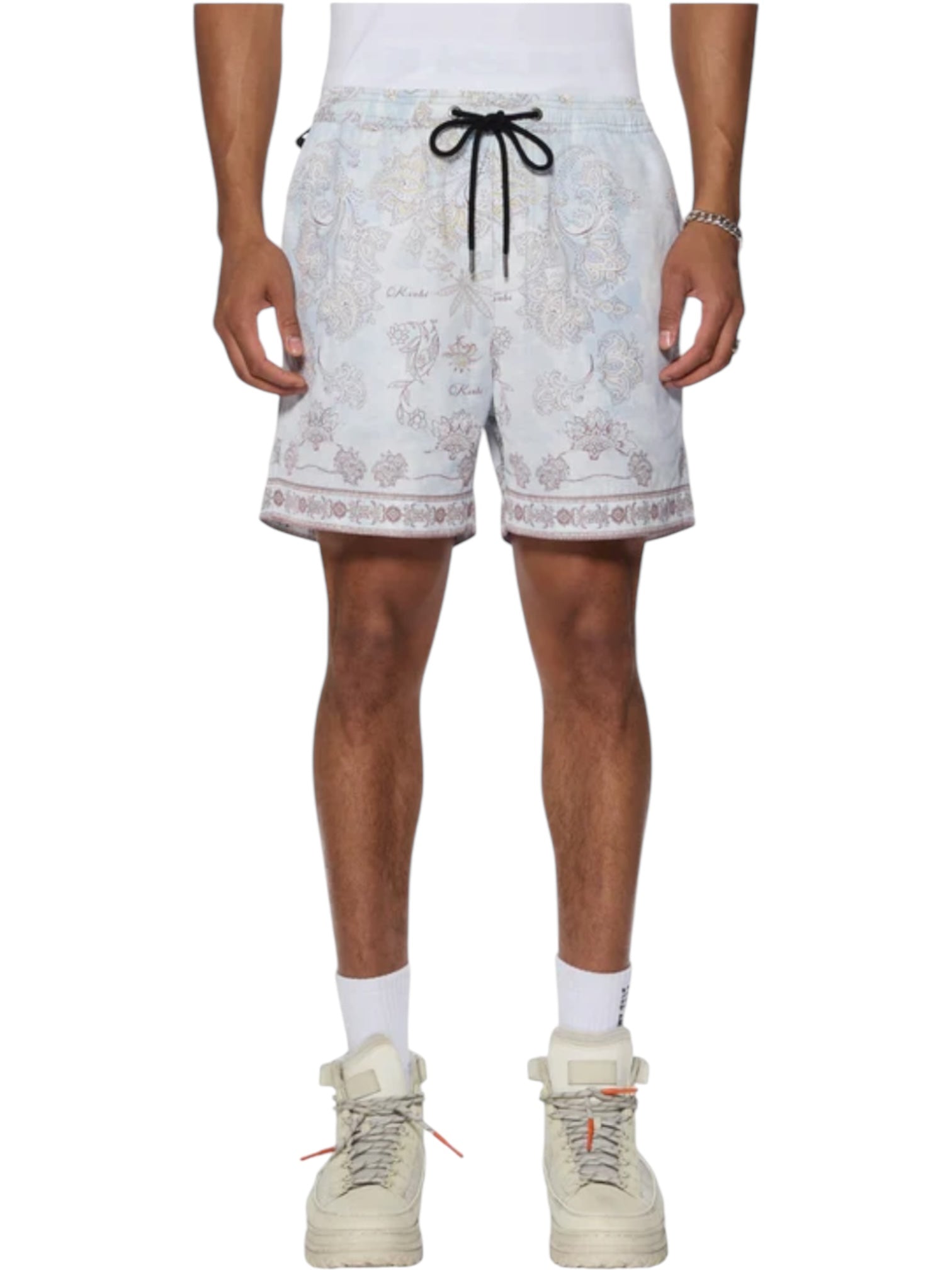 A person wearing KSUBI Eternity Boardshort Multi with paisley print, a black drawstring, white socks, and white high-top sneakers stands against a plain background.