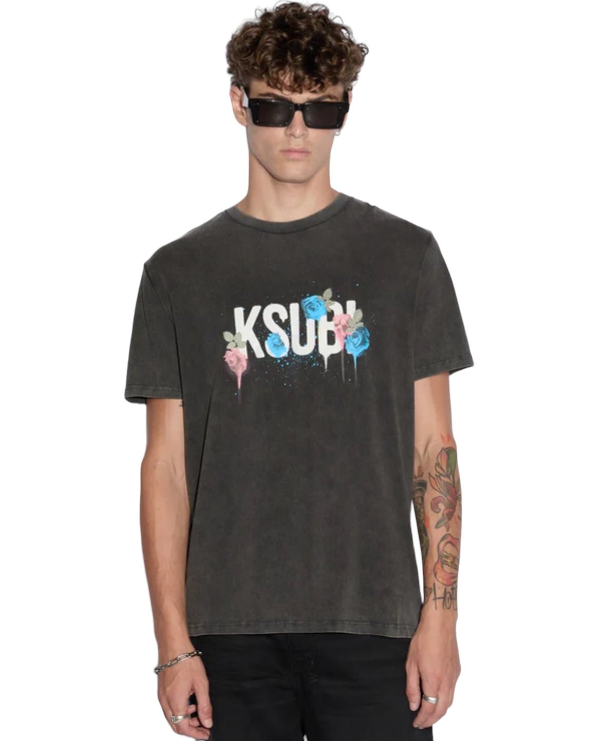 A person wearing sunglasses and the Ksubi Graff Rose Kash Tee in Acid Grey, paired with black pants, confidently stands against a plain white background.