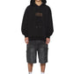 A person wears the KSUBI Kingdom Biggie Hoodie in jet black with black baggy shorts, white socks, and black sneakers, standing against a white background.