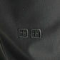 A close-up of the black Ksubi Melrose Suit Pant by KSUBI displays two small embossed square symbols with stylized cross designs.