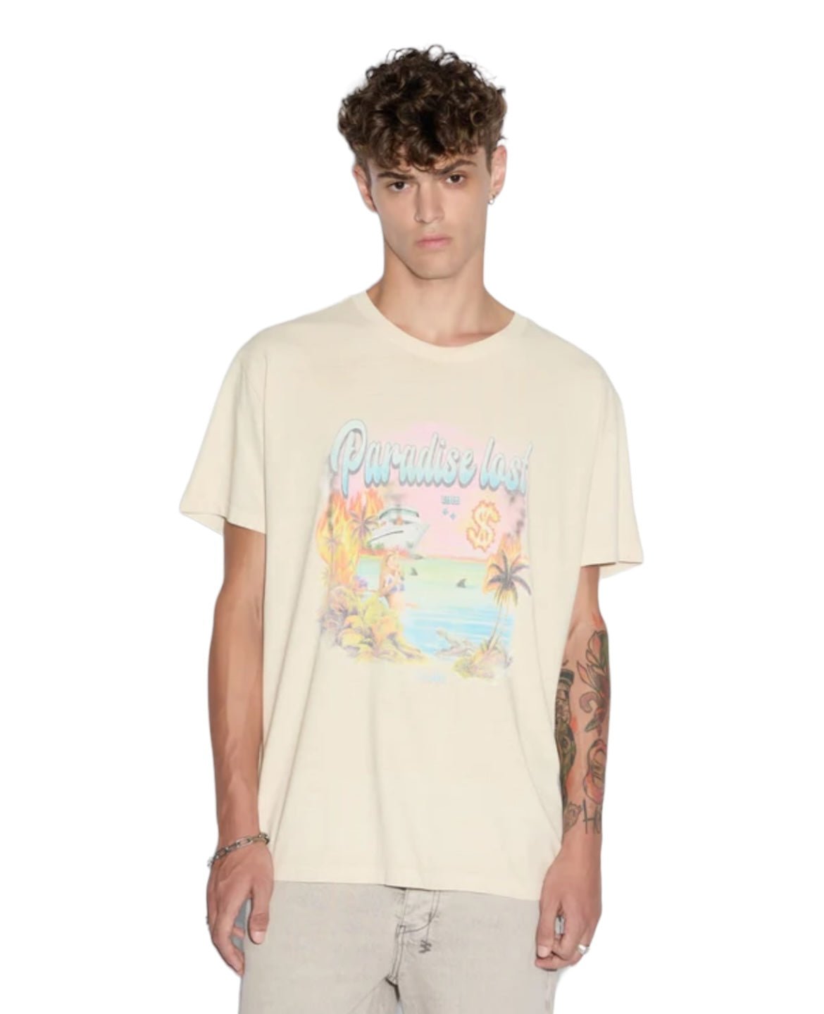 A man stands wearing the KSUBI PARADISE BIGGIE TEE DUSTY DESERT TAN, a premium cotton jersey in tan color, featuring a "Paradise Lost" design with a beach scene showcasing palm trees and flamingos. He has a tattoo on his left forearm.