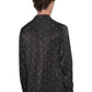 A person with curly hair wears the Ksubi Polka Plus Ls Shirt Black by KSUBI, featuring small white dots on polyester. The shirt's long sleeves and button-down style pair well with their black pants as they stand facing away from the viewer.