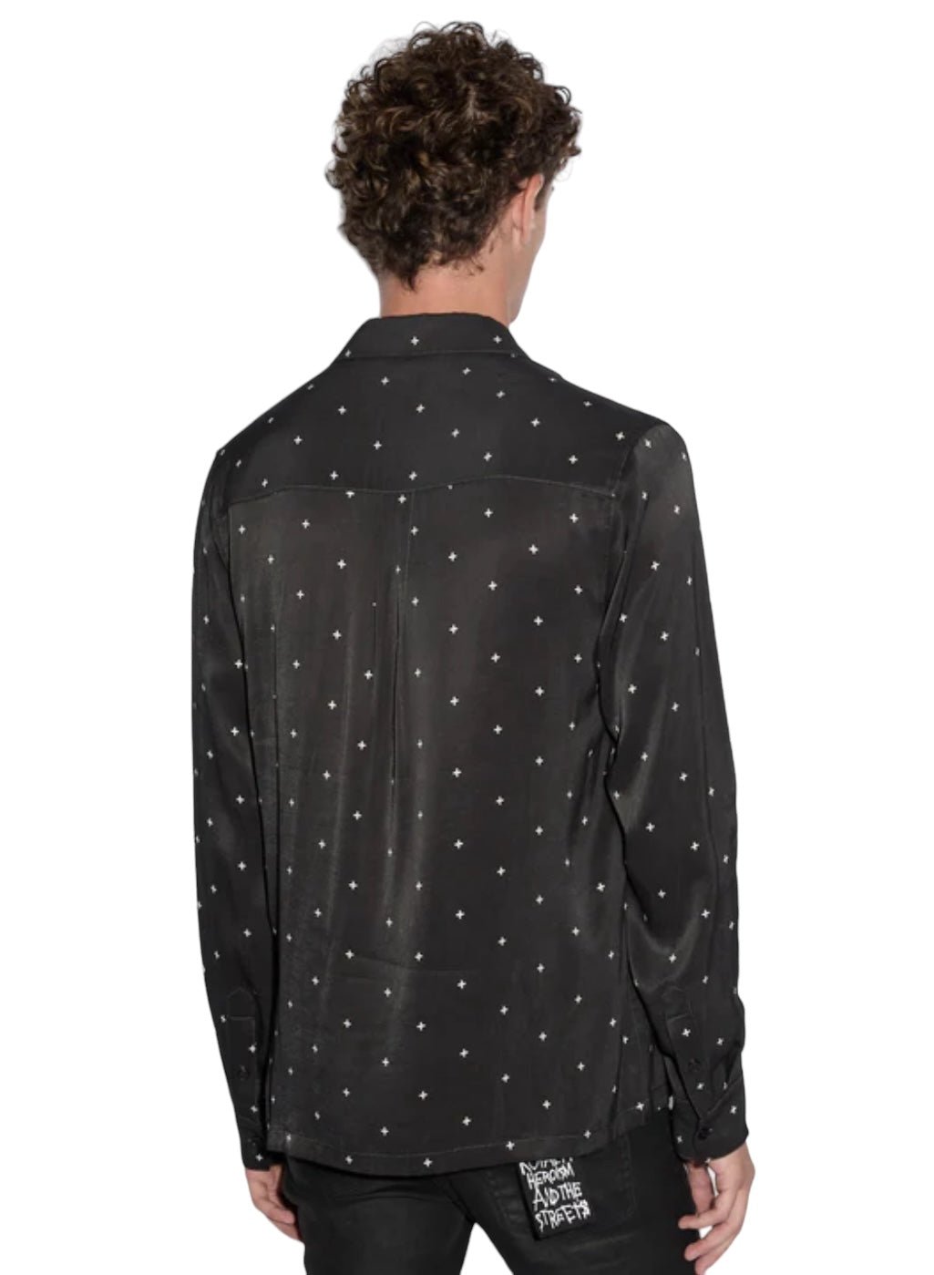 A person with curly hair wears the Ksubi Polka Plus Ls Shirt Black by KSUBI, featuring small white dots on polyester. The shirt's long sleeves and button-down style pair well with their black pants as they stand facing away from the viewer.