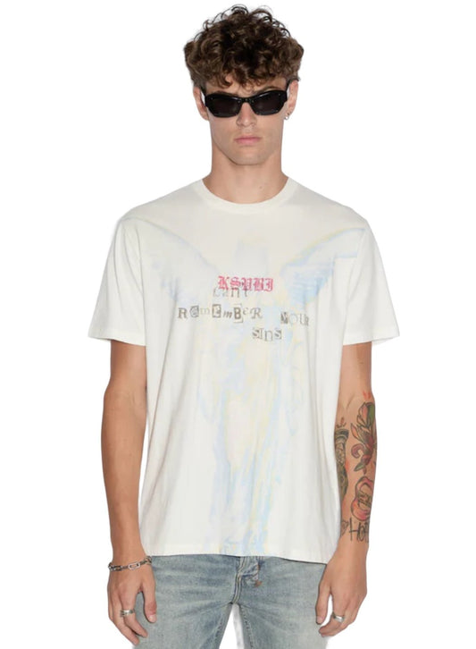 A man with curly hair and sunglasses is seen wearing the KSUBI SINNERS KASH SS TEE VINTAGE WHITE, a vintage-style T-shirt from the brand KSUBI featuring pastel graphics and text, made from premium cotton. He pairs it with light blue jeans and displays tattoos on his left arm.