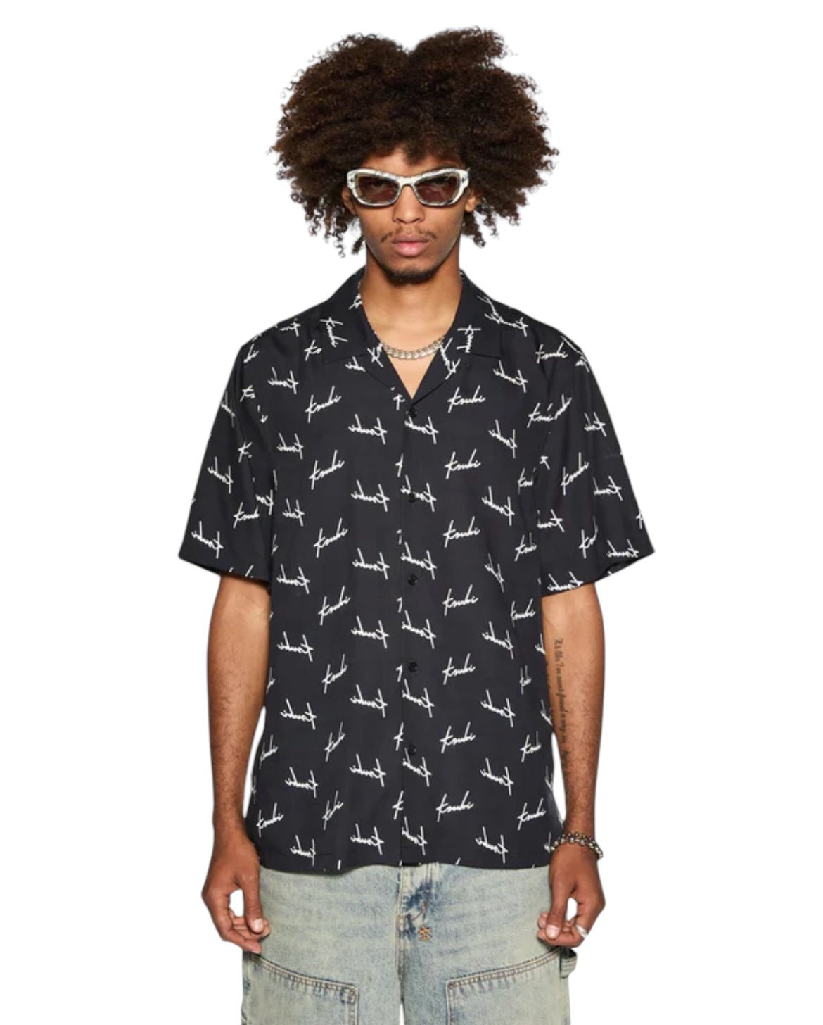 A person wearing the Ksubi Skript Resort Resort SS Shirt in black, crafted from premium Tencel with Ksubi branding, sunglasses, and light-colored pants stands against a white background.