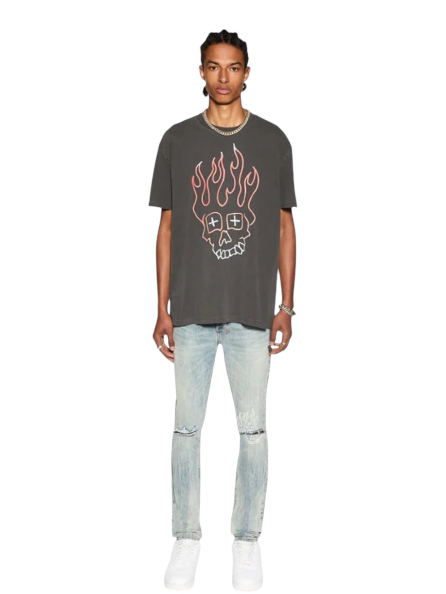 A person stands facing forward in a Ksubi Skull Biggie Ss Tee Faded Blk from KSUBI, showcasing a flaming skull graphic. They pair it with light ripped jeans and white shoes, all set against a plain white backdrop.