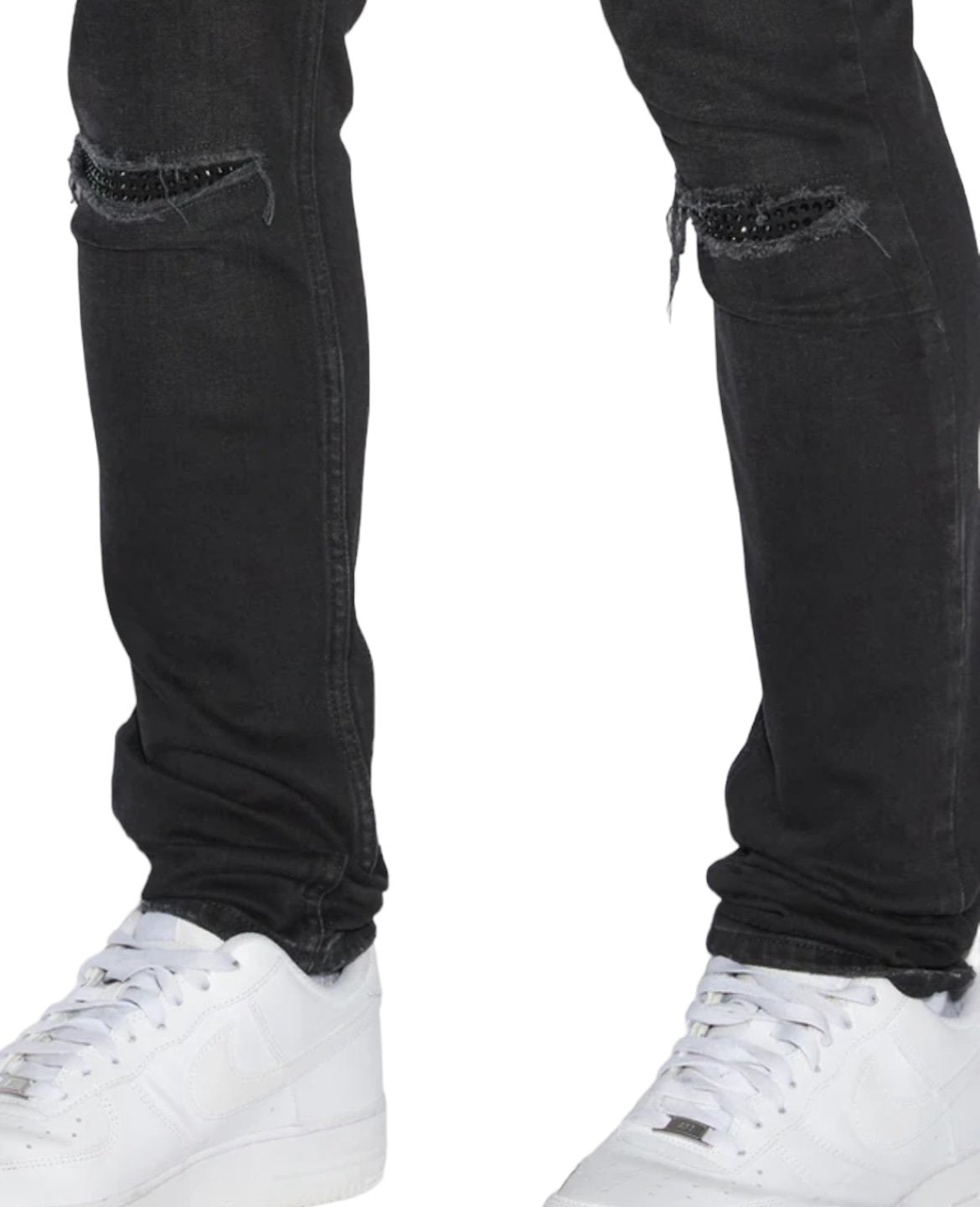 Close-up of a person's legs wearing black stretch denim skinny jeans and white sneakers, capturing the edgy style synonymous with KSUBI KSUBI VAN WINKLE APEX KRYSTAL REPAIR BLACK.