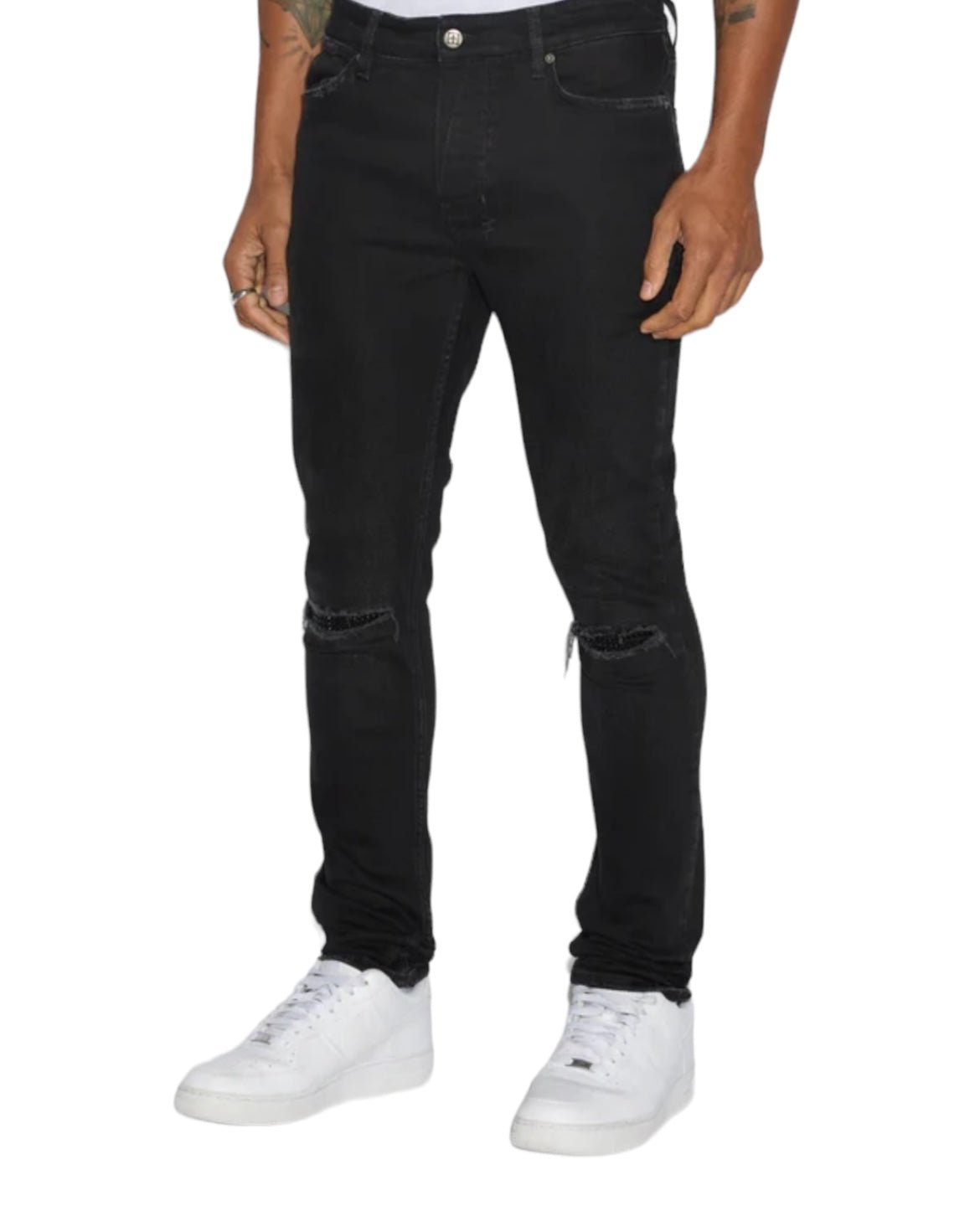 Man wearing KSUBI KSUBI VAN WINKLE APEX KRYSTAL REPAIR BLACK stretch denim skinny jeans and white sneakers, standing with hands by his sides. Upper body is not visible.