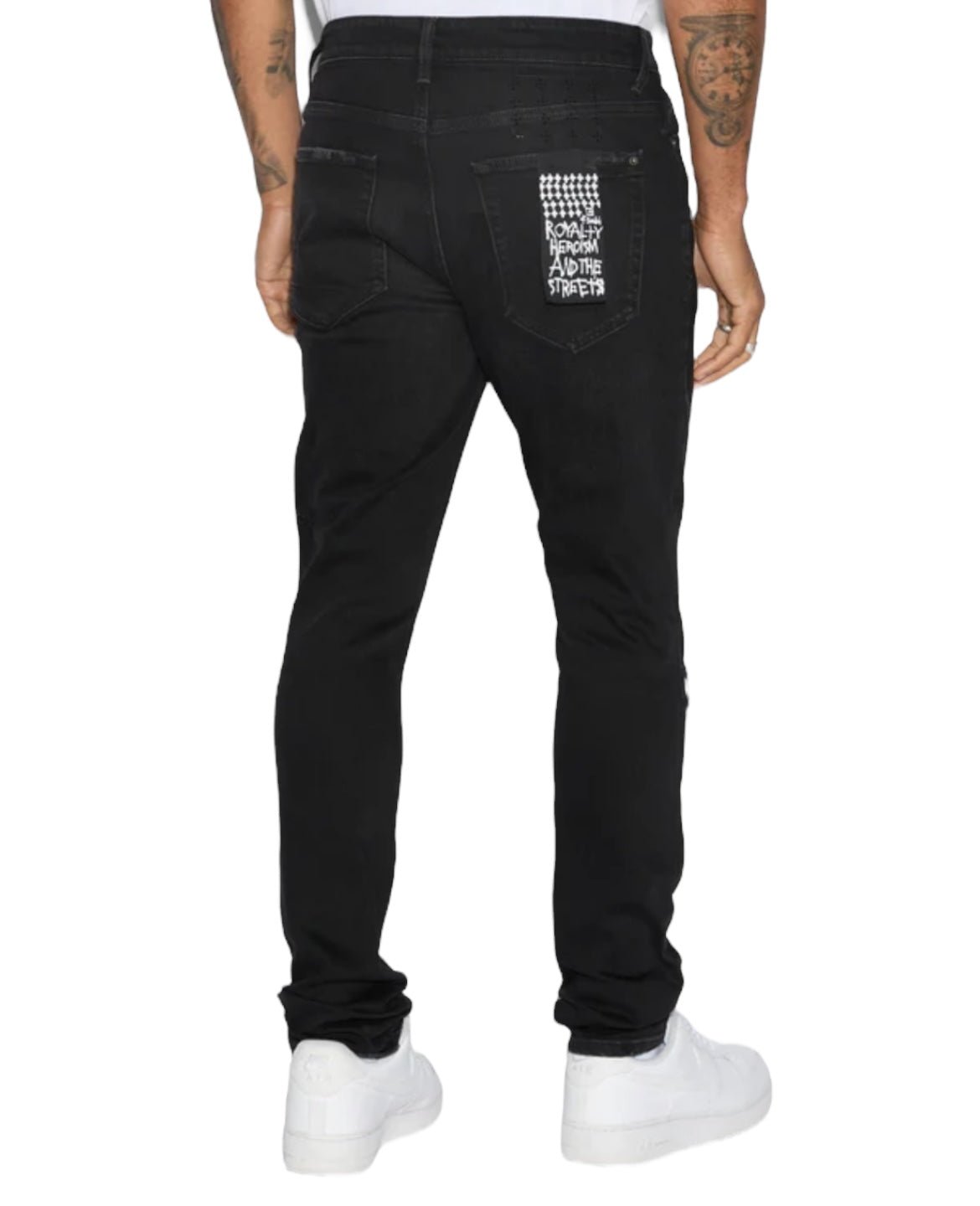 A person wearing KSUBI VAN WINKLE APEX KRYSTAL REPAIR BLACK jeans with a patch reading "Hooligans Against the Pressure and the Struggles" on the back pocket, paired with white sneakers.