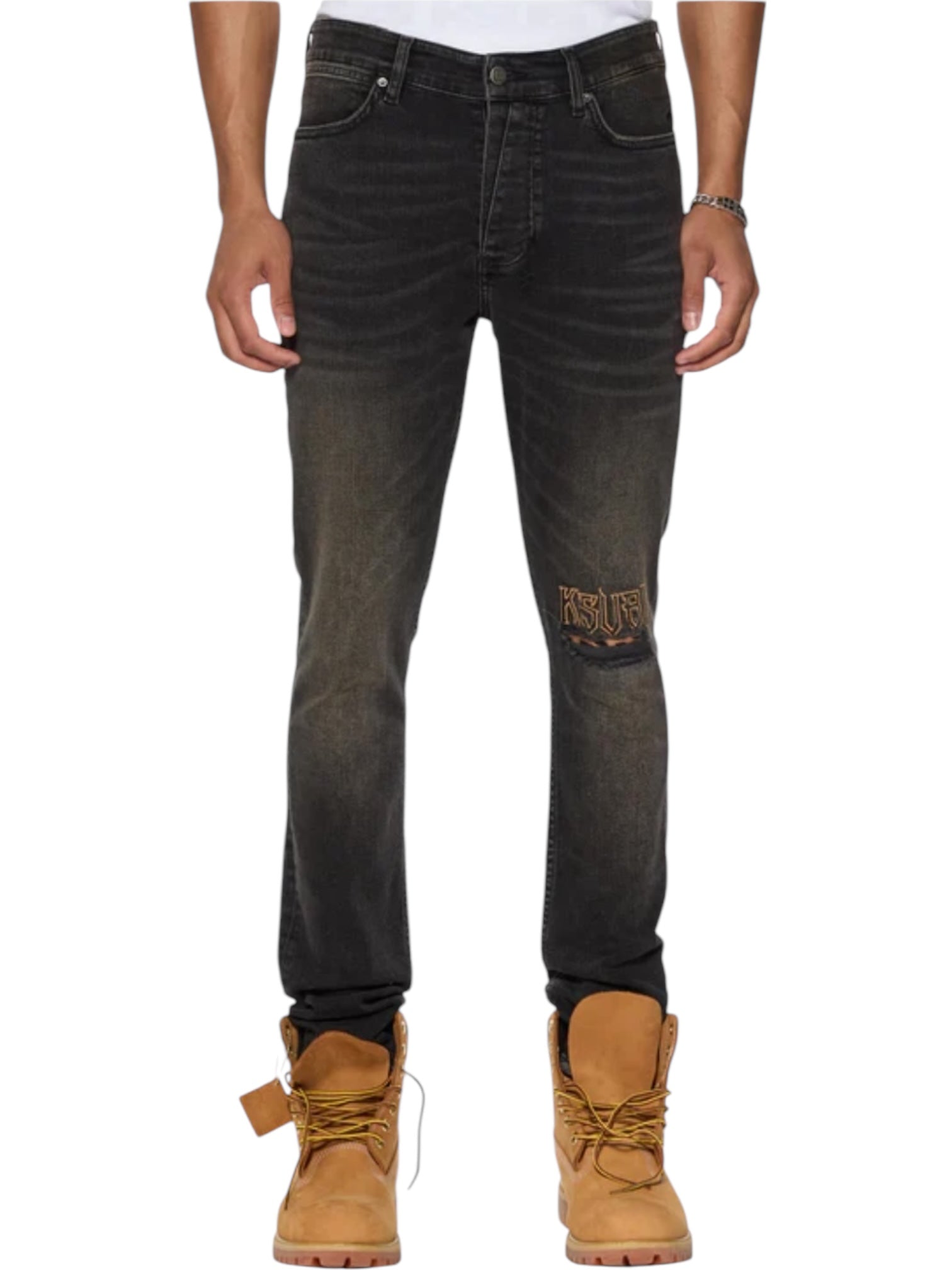 Wearing KSUBI Van Winkle Kingdom Repair Black jeans with a knee patch, tan work boots, and a white shirt. Only the lower torso and legs are shown; the jeans display a small Ksubi logo.