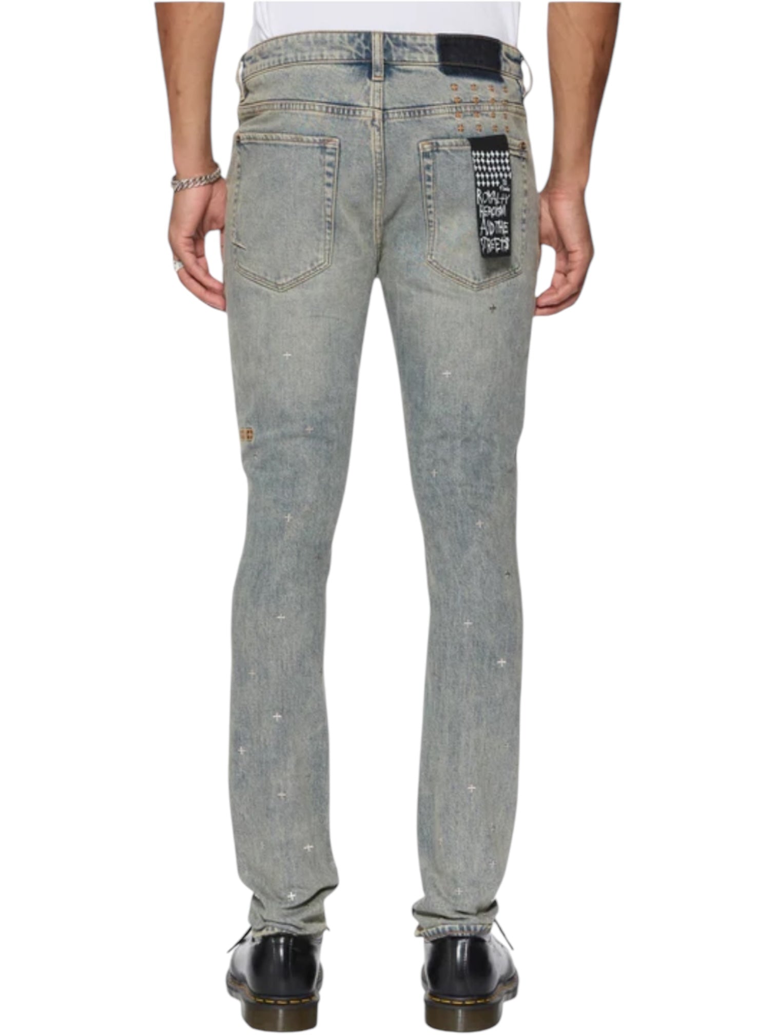 Person wearing KSUBI Van Winkle Stagelight Metalik Denim—light blue skinny jeans with Ksubi hardware and a black and white patch on the right back pocket—paired with black shoes and a white shirt, standing with their back to the camera.