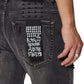 Close-up of the back pocket on KSUBI's ksubi Van Winkle Torqued Chamber Black jeans, featuring a "ROYALTY HEROISM AND THE STREETS" patch and worn by someone with a ring, highlighting premium comfort stretch.