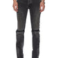 A person wearing KSUBI Van Winkle Torqued Chamber Black jeans with visible knee seams and black square-toe boots, standing against a white background. These jeans provide premium comfort stretch for all-day wear.