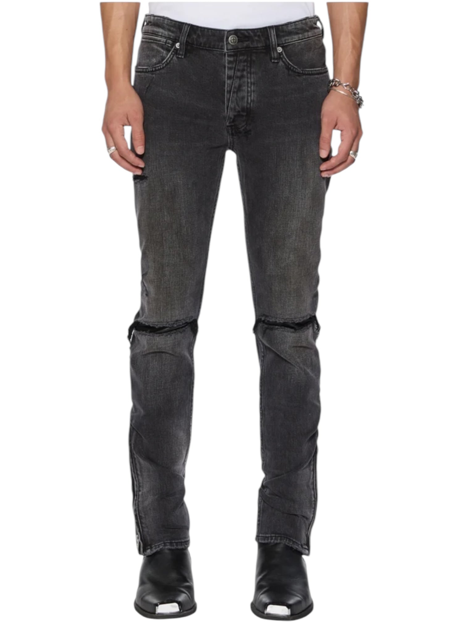 A person wearing KSUBI Van Winkle Torqued Chamber Black jeans with visible knee seams and black square-toe boots, standing against a white background. These jeans provide premium comfort stretch for all-day wear.