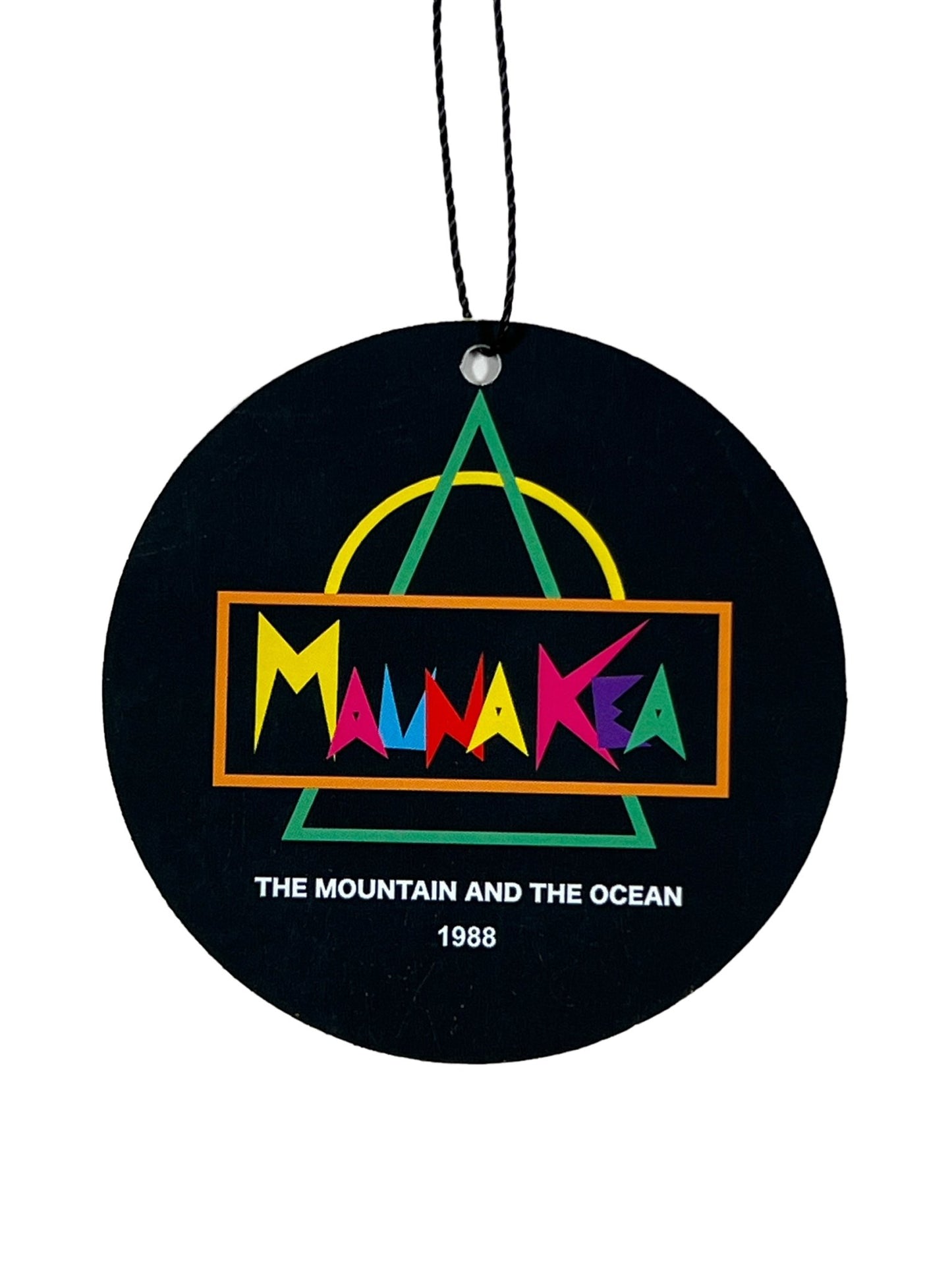 Round black tag with colorful text "Maunakea" above "The Mountain and The Ocean 1988" and geometric shapes in the background, attached to a string—perfect for your MAUNA-KEA MAUNA-KEA MKE100-04 HERITAGE TEE W SCREEN PRINT PINK.
