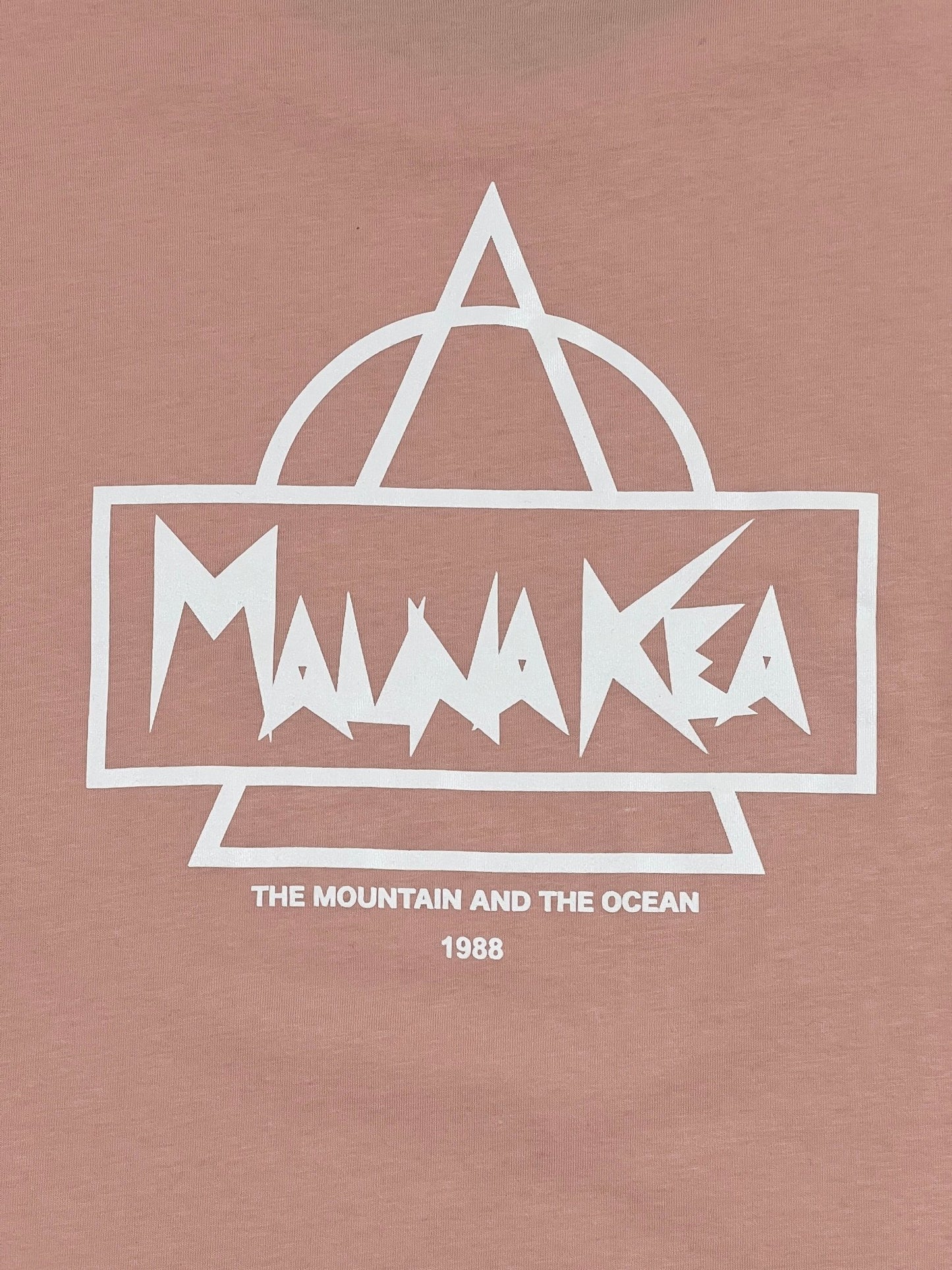 Text-based design on a pink background. The text reads: "Mauna Kea" with additional text below: "The Mountain and the Ocean" and "1988" in smaller font. Geometric shapes surround the main text. This MAUNA-KEA MAUNA-KEA MKE100-04 HERITAGE TEE W SCREEN PRINT PINK is made from 100% cotton for ultimate comfort.