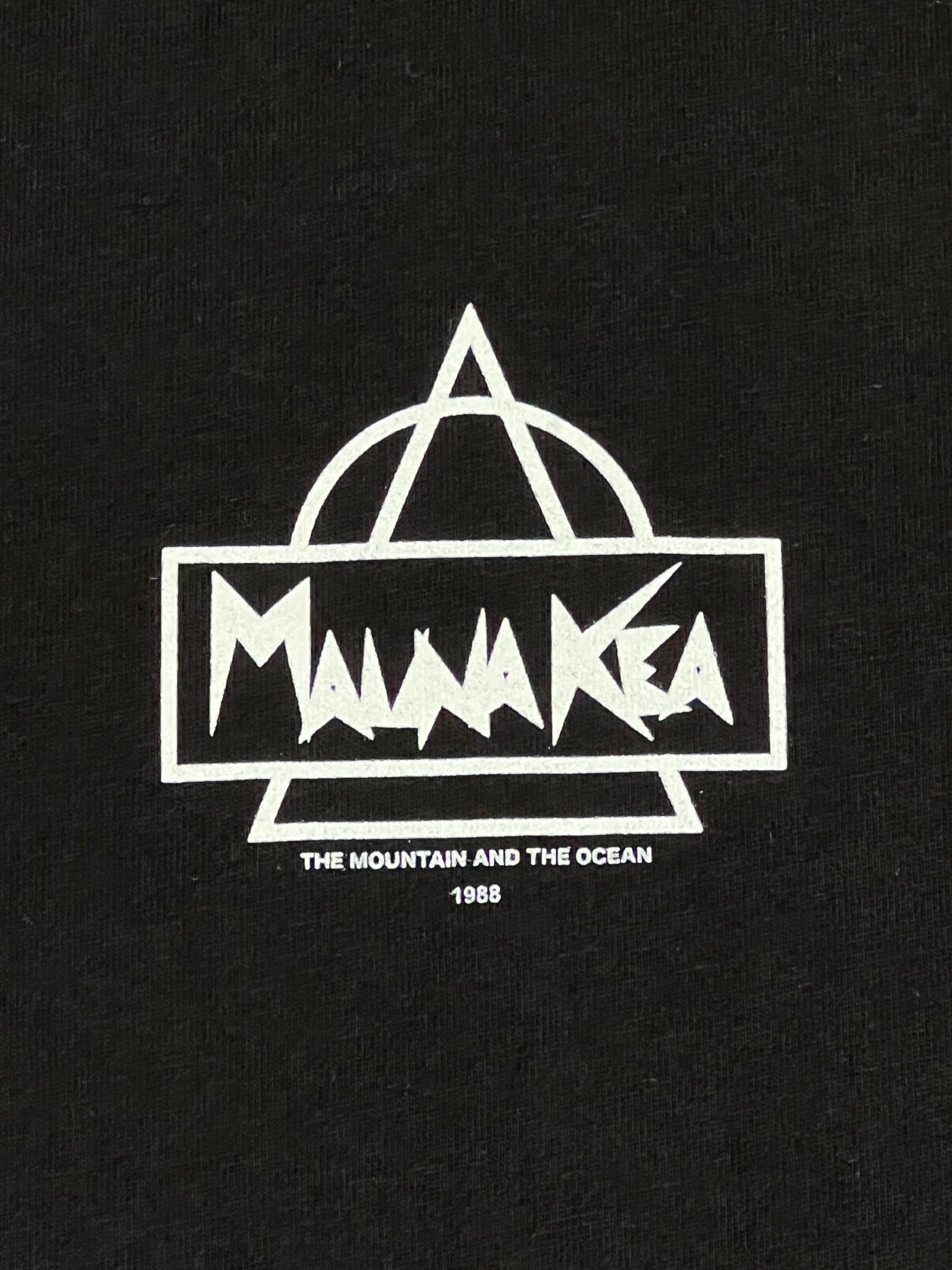 MAUNA-KEA MKE100-999 HERITAGE TEE W SCREEN PRINT BLK featuring a white graphic of a stylized mountain peak and ocean waves with the text "Maunakea - the mountain and the ocean 1988" on a black background. Made of 100% Cotton.