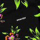 A close-up of a MAUNA-KEA MKU142-FL floral shirt in vibrant green, orange, and pink colors on a black background. The text "mauna kea" is printed in white.
