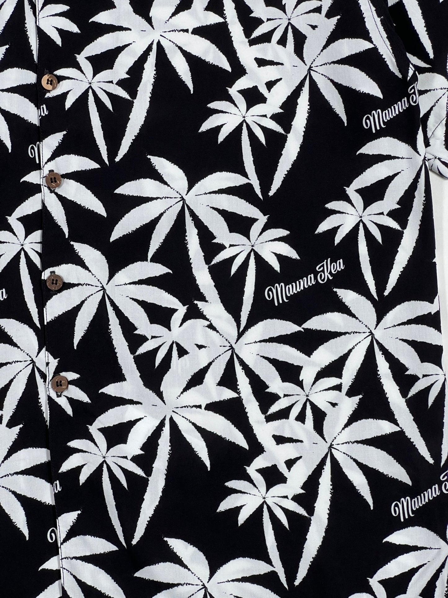 The Mauna-Kea Mku142-Pm1 Allover Print Shirt in black features short sleeves adorned with white graphic palm tree patterns and the words "Mauna Kea" throughout. Crafted in Italy by MAUNA-KEA, it brings a stylish touch of tropical elegance.