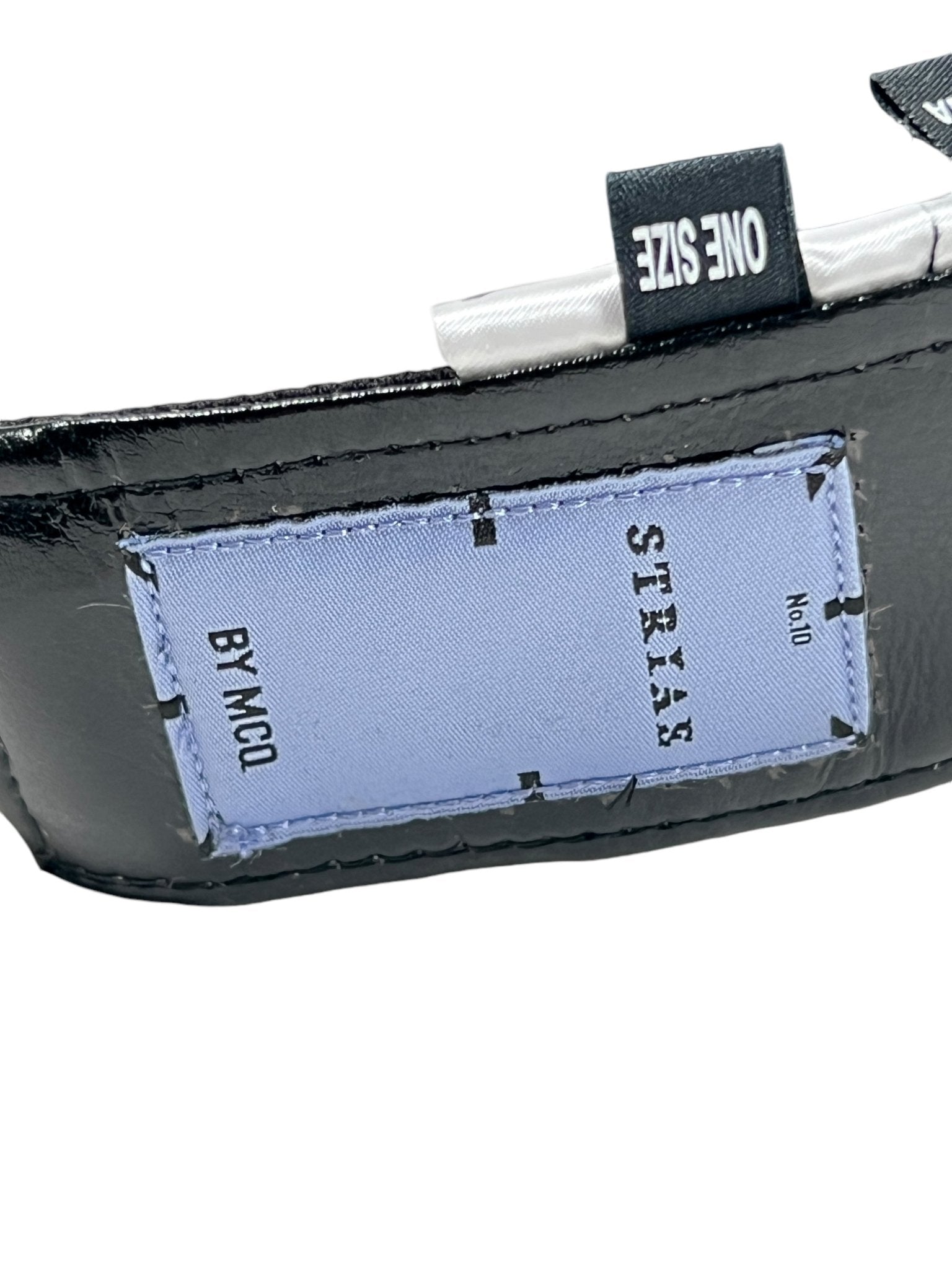 Close-up of a leather strap with a light blue fabric tag labeled "MCQ BY MCQUEEN," attached to a visor cap, alongside a paper tag reading "ONE SIZE." Product: Mcq By Mcqueen 692287Rgc96 Handsy Visor Black.