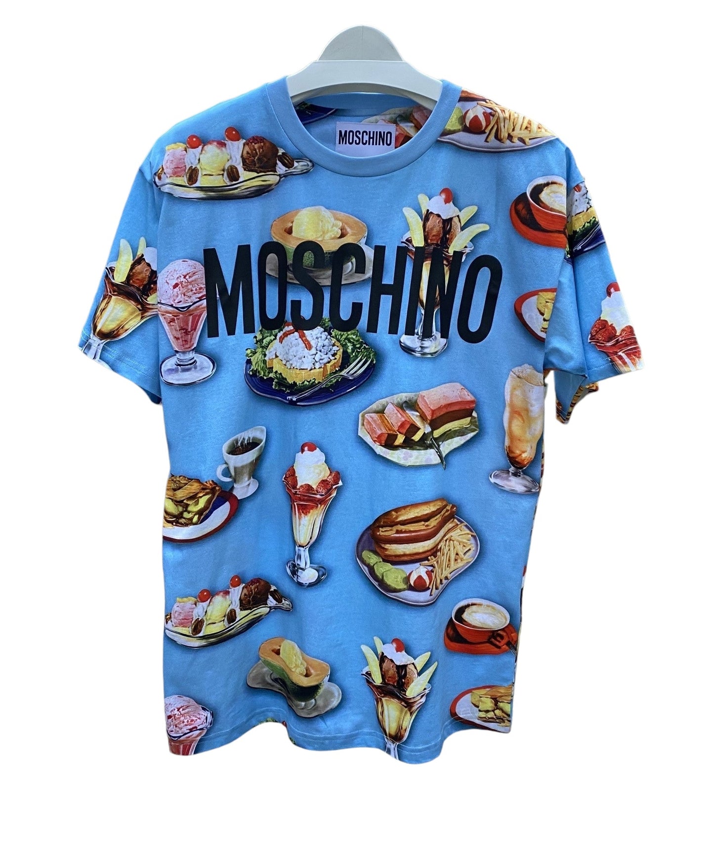 The Moschino 0718-Cotton Jersey Fantasy Print Light Blue T-shirt by MOSCHINO, made in Italy, features a vibrant print of colorful food illustrations—desserts and meals—displayed on a hanger.