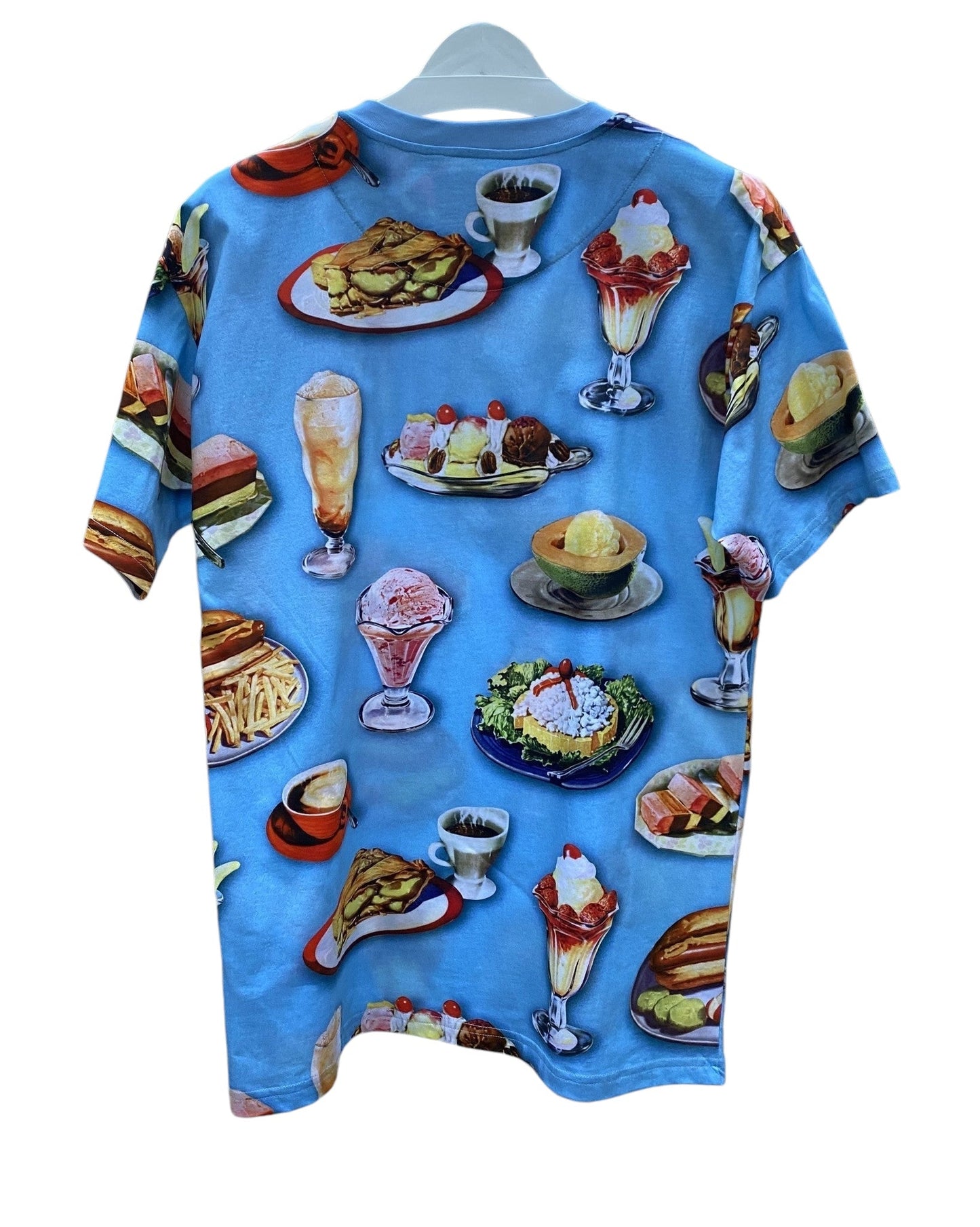 The Moschino 0718-Cotton Jersey Fantasy Print Light Blue t-shirt features a fun print of burgers, fries, ice cream, and salads on a white hanger. Made in Italy, it's perfect for fashion lovers with a playful side.