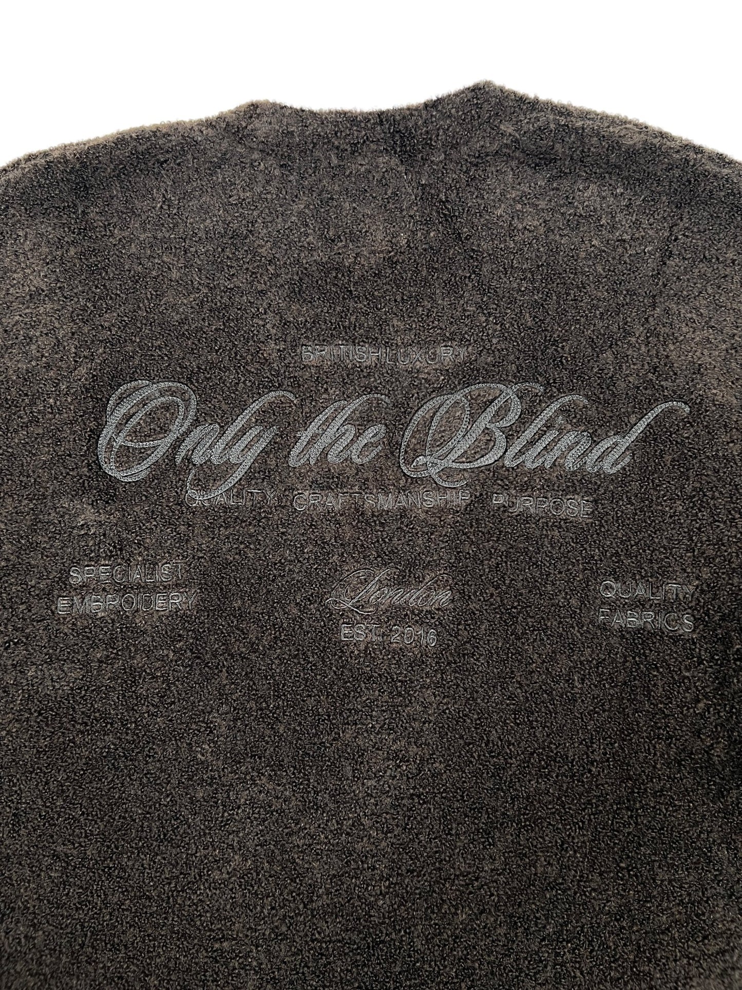 The Only The Blind OTB-K1629 Brown Studio Dept. Cardigan by ONLY THE BLIND features textured brown fabric and embroidered phrases such as “Only The Blind,” “British Luxury,” “Quality Fabrics,” and “Specialist Embroider.”.
