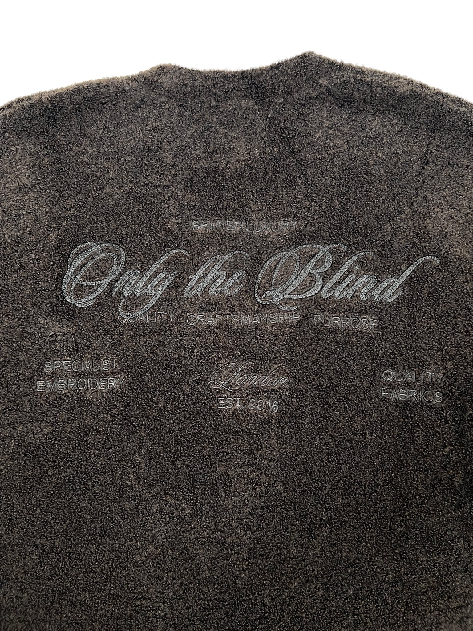 The Only The Blind OTB-K1629 Brown Studio Dept. Cardigan by ONLY THE BLIND features textured brown fabric and embroidered phrases such as “Only The Blind,” “British Luxury,” “Quality Fabrics,” and “Specialist Embroider.”.