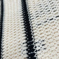 A close-up of a crocheted fabric with alternating beige and black vertical stripes reveals intricate looping patterns, showcasing the meticulous craftsmanship of the Only The Blind OTB-SH1520 Desert Stripe Crochet Shirt by ONLY THE BLIND.