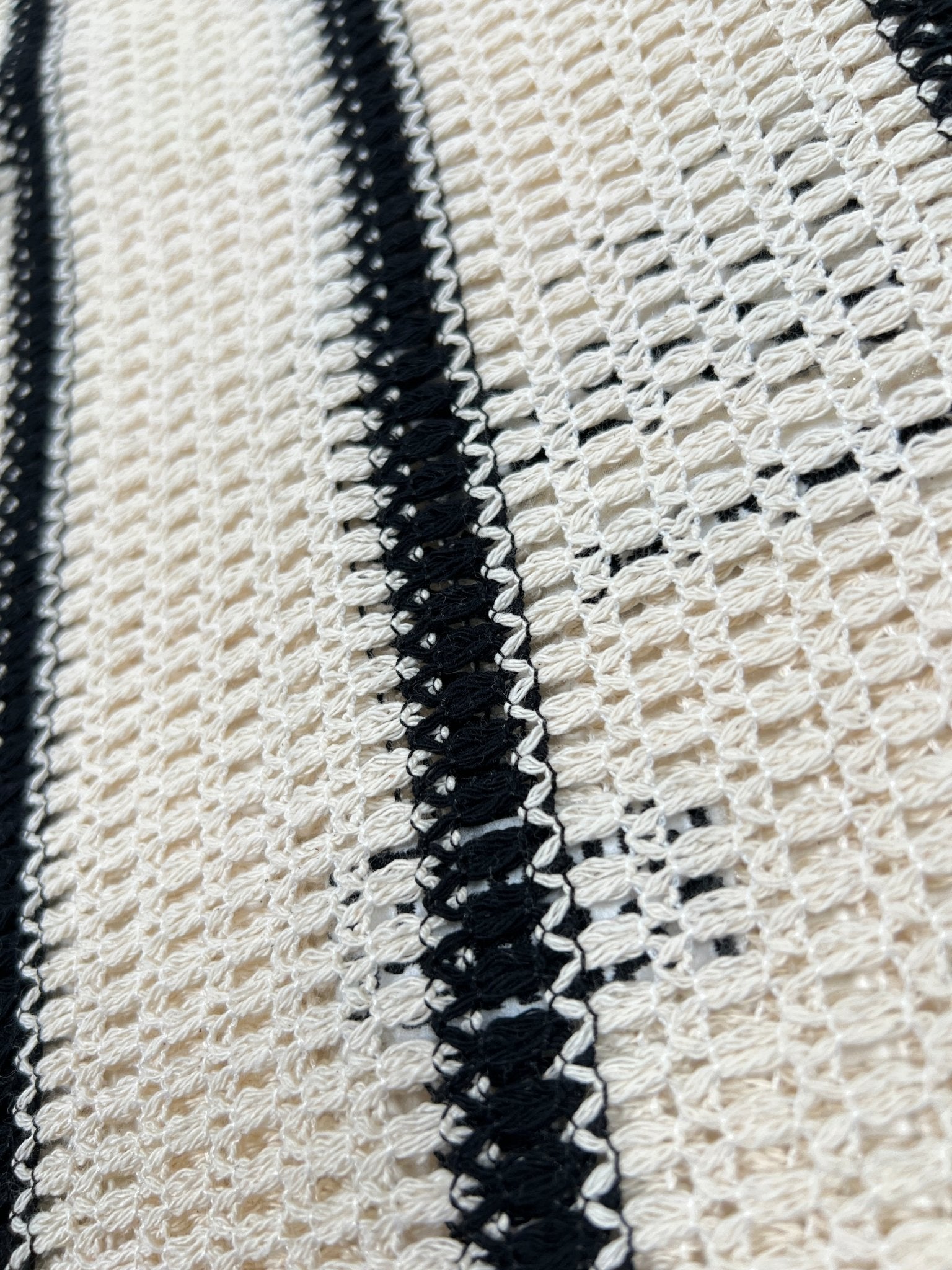 A close-up of a crocheted fabric with alternating beige and black vertical stripes reveals intricate looping patterns, showcasing the meticulous craftsmanship of the Only The Blind OTB-SH1520 Desert Stripe Crochet Shirt by ONLY THE BLIND.