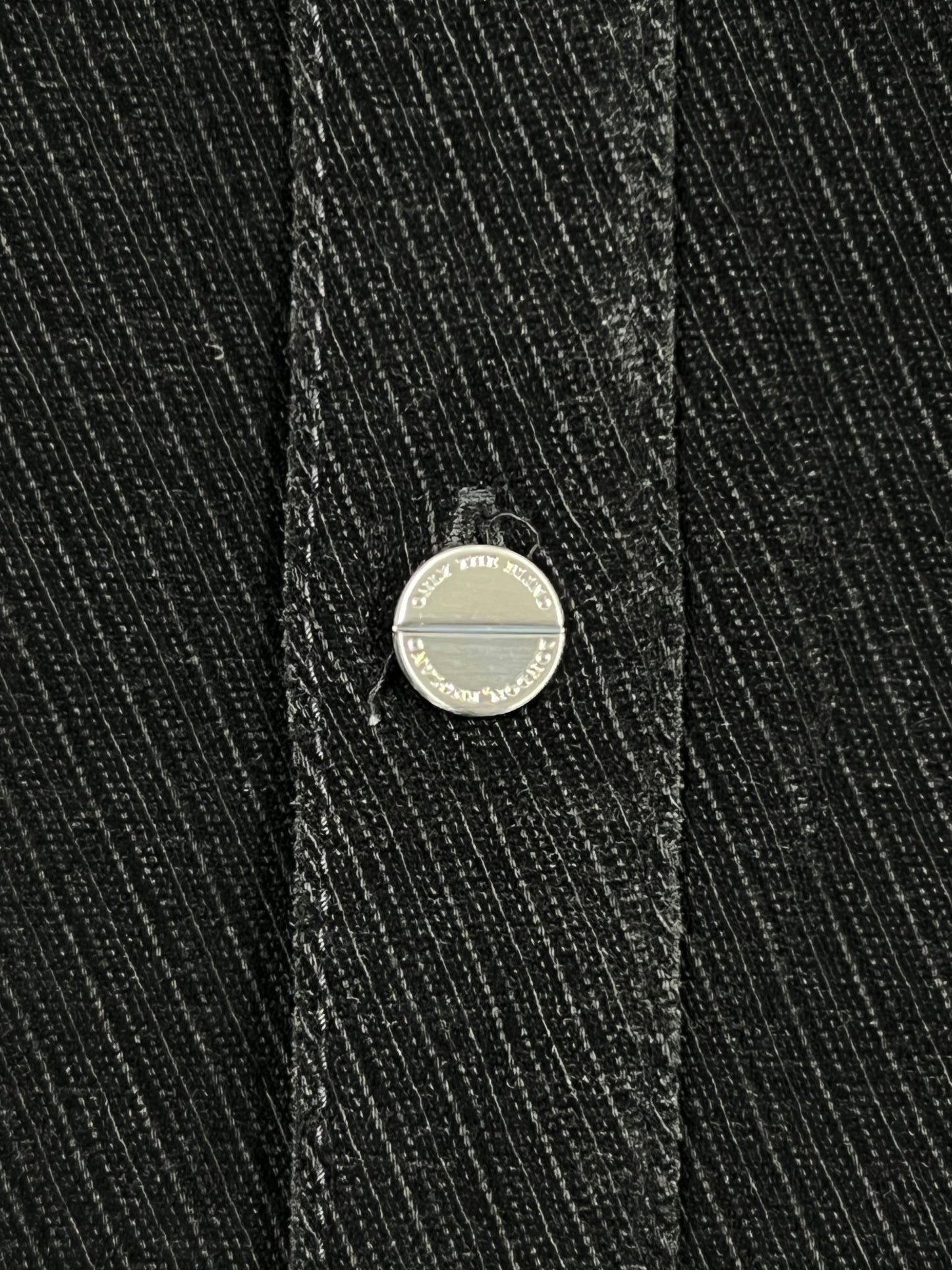 Close-up of a metal button with engraved text on the edge, set on dark, diagonally striped fabric—part of the Probus Only The Blind OTB-SH1572 Noir Heritage Shirt Black.