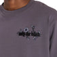 A person wearing an ONLY THE BLIND Wildflower T-shirt in purple, featuring blackberry floral embroidery and the text "only the blind" across the chest.
